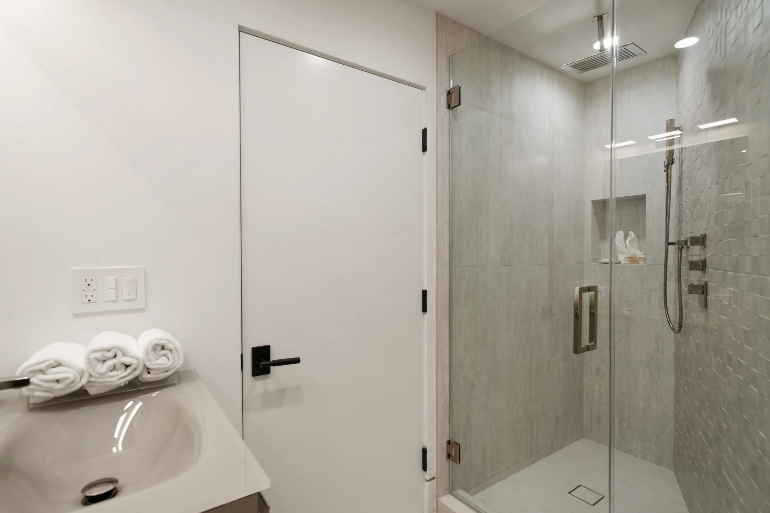 Ensuite shower room with glass-walled rain shower and rolled towels on the vanity