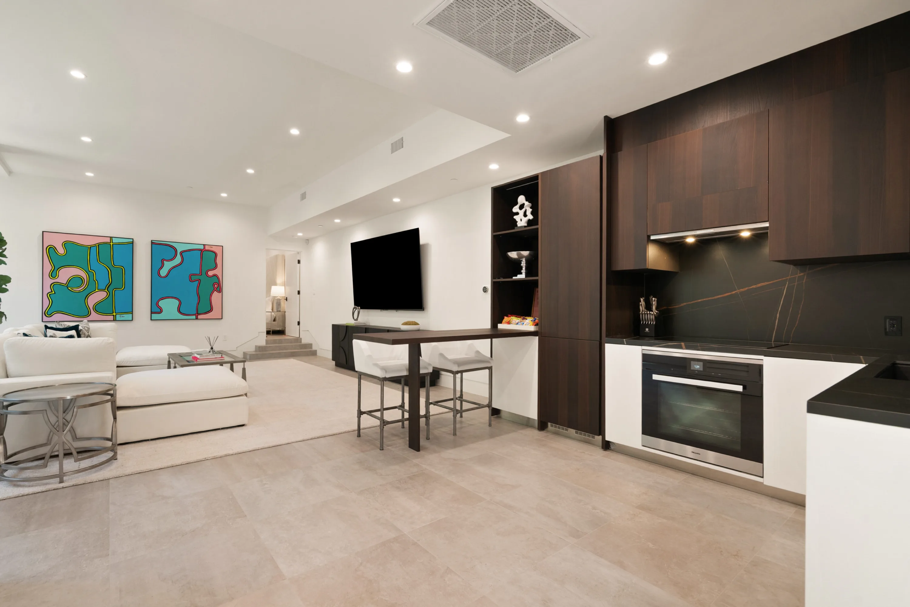 Lower-level lounge with kitchenette, bar-height counter and wall-mounted TV beside pop-art panels