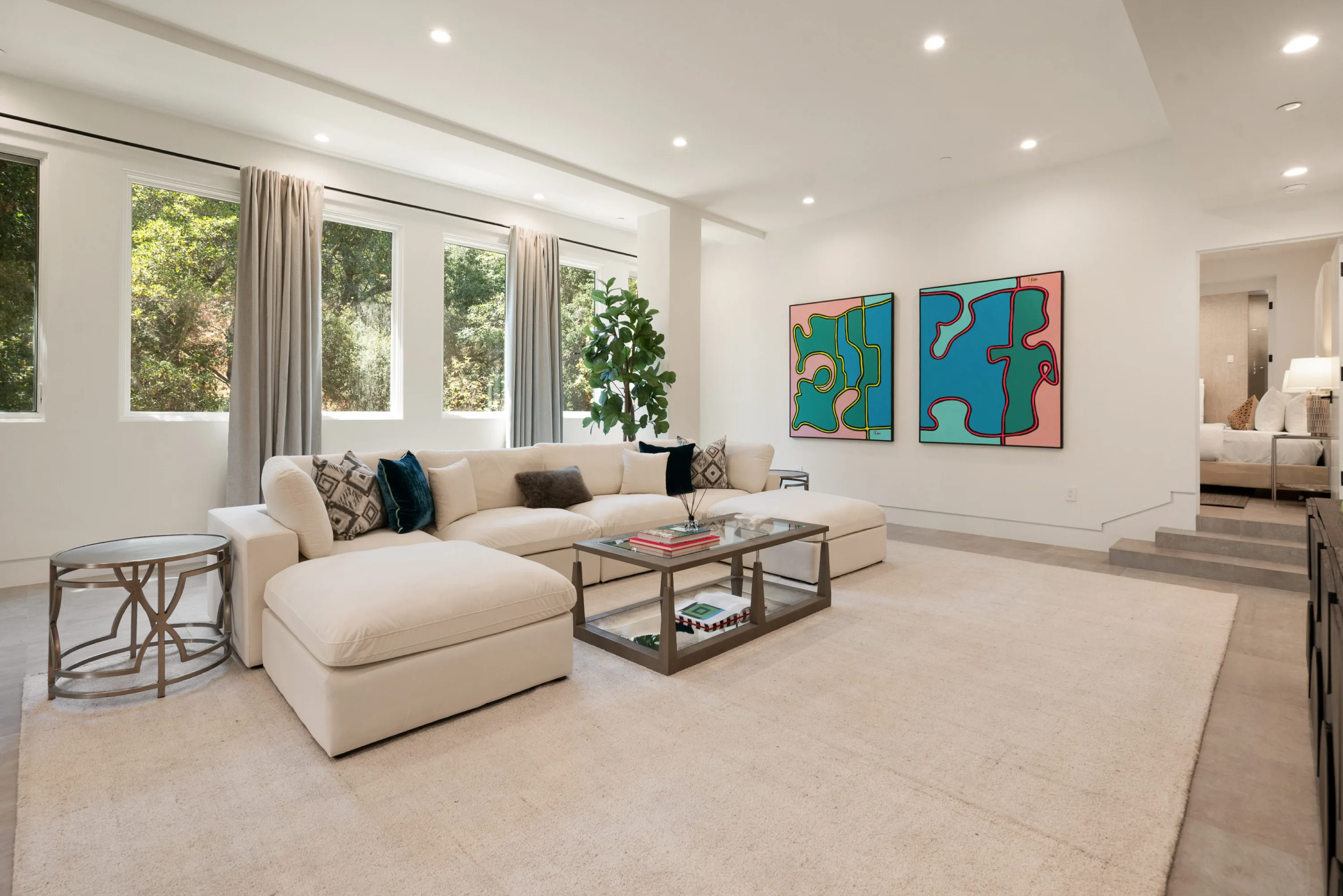 Family room with deep sectional, tall windows onto greenery and a pair of graphic canvases