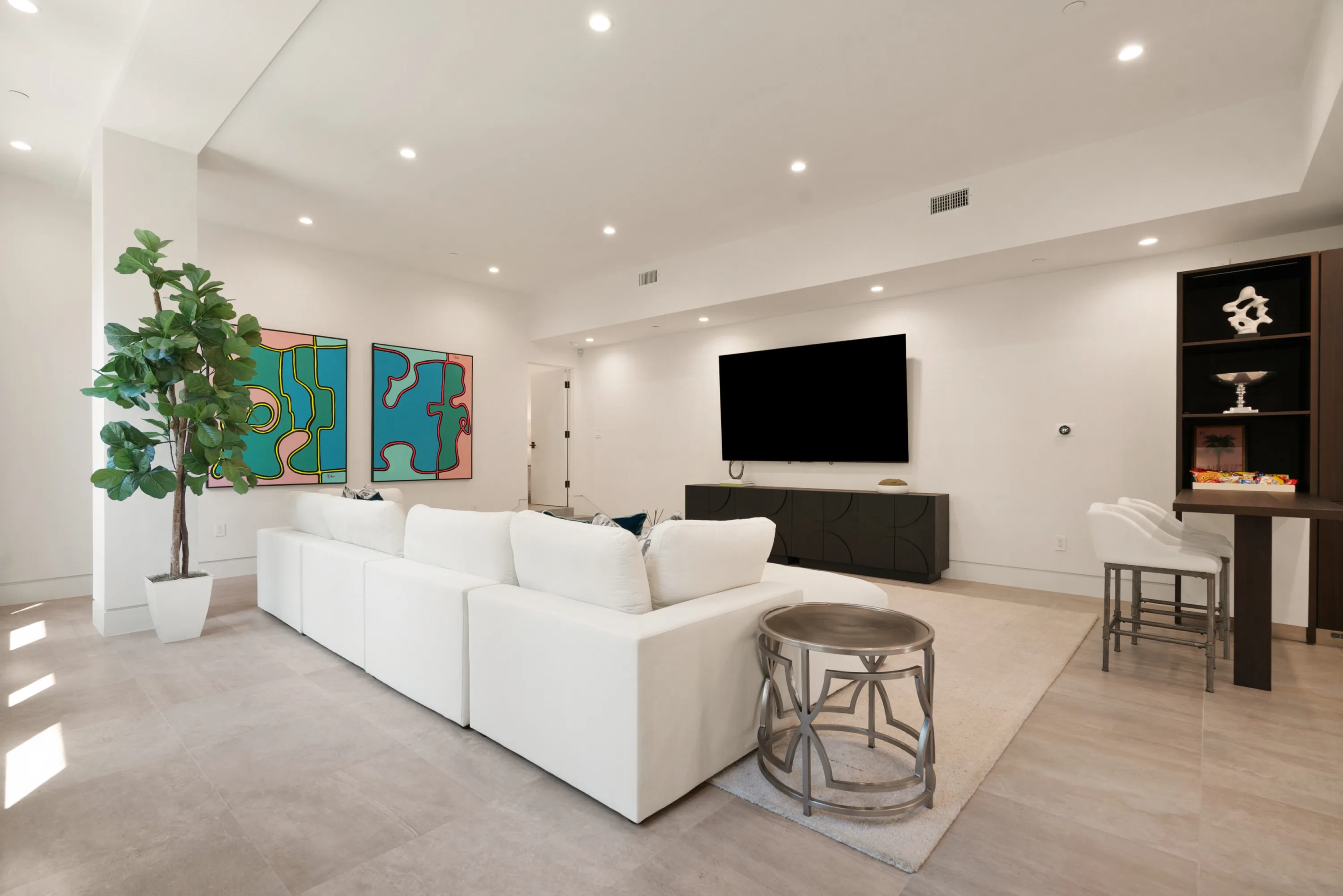 Media lounge seen across the sectional toward the big-screen TV, credenza and bar stools