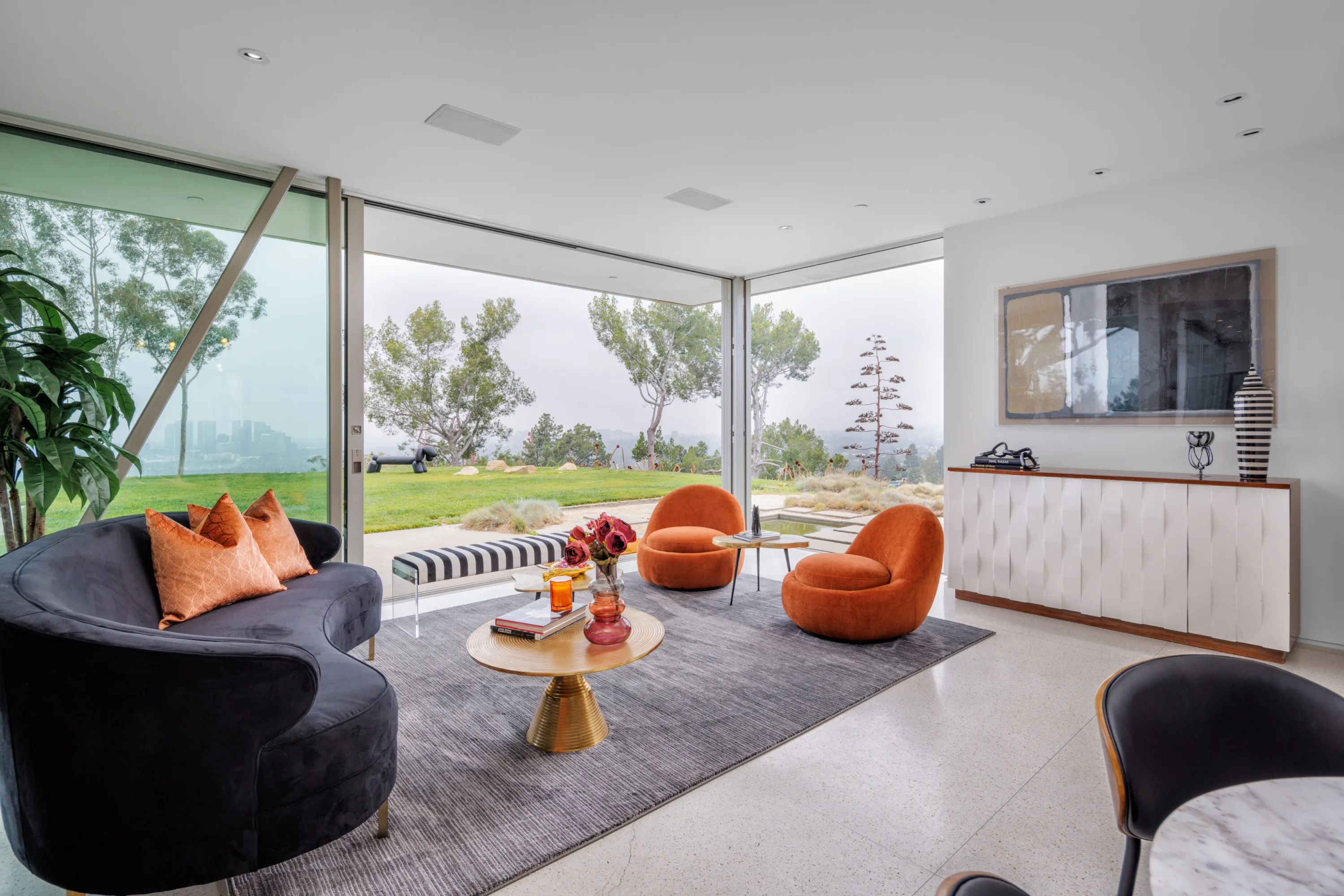 Living room with curved navy sofa and orange swivel chairs facing sliding glass onto the lawn