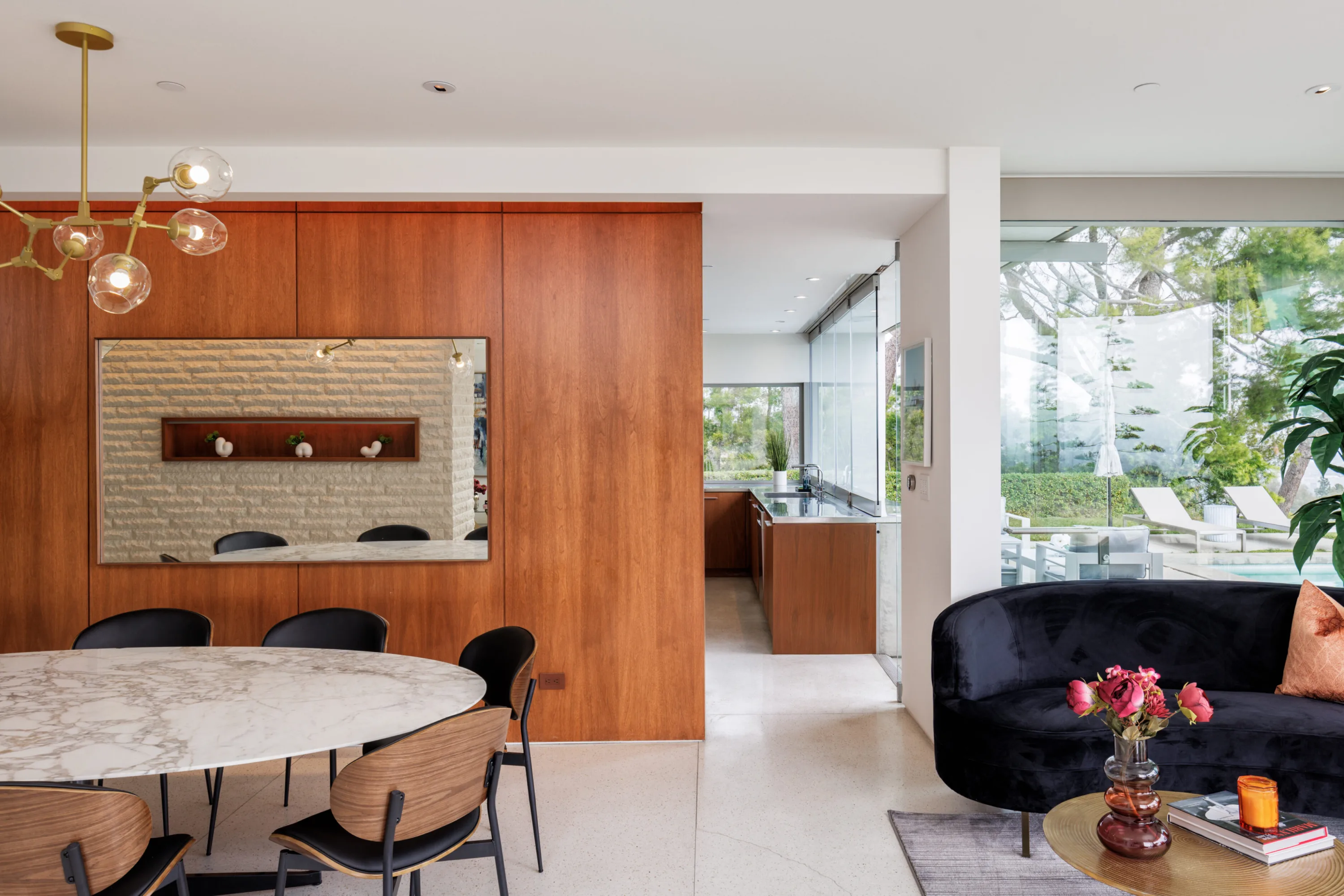 Dining area against a walnut wall with mirror, sightline through to the kitchen and poolside loungers