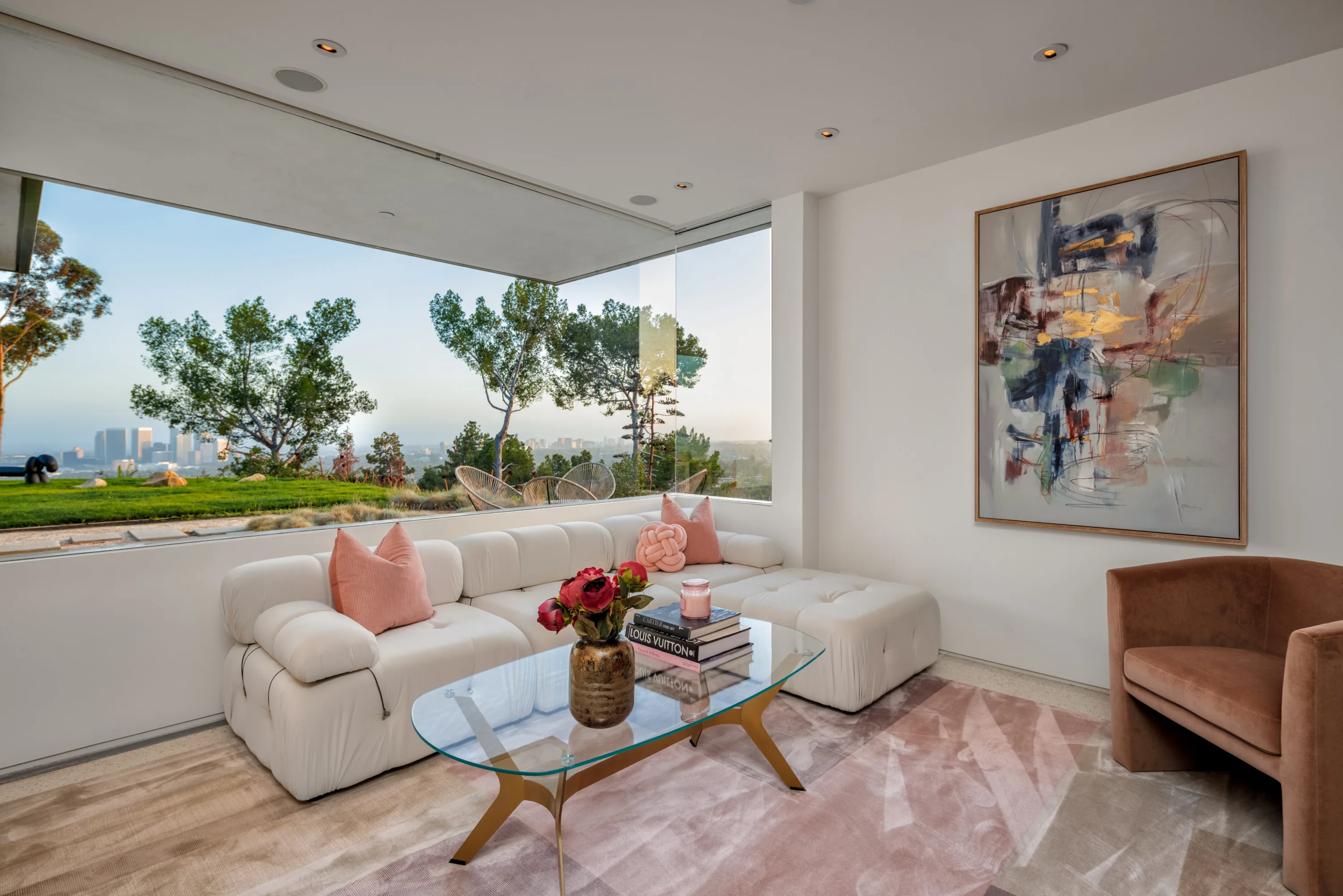 Sitting room with cream tufted sectional, abstract canvas and a picture window over the lawn; book reads Louis Vuitton