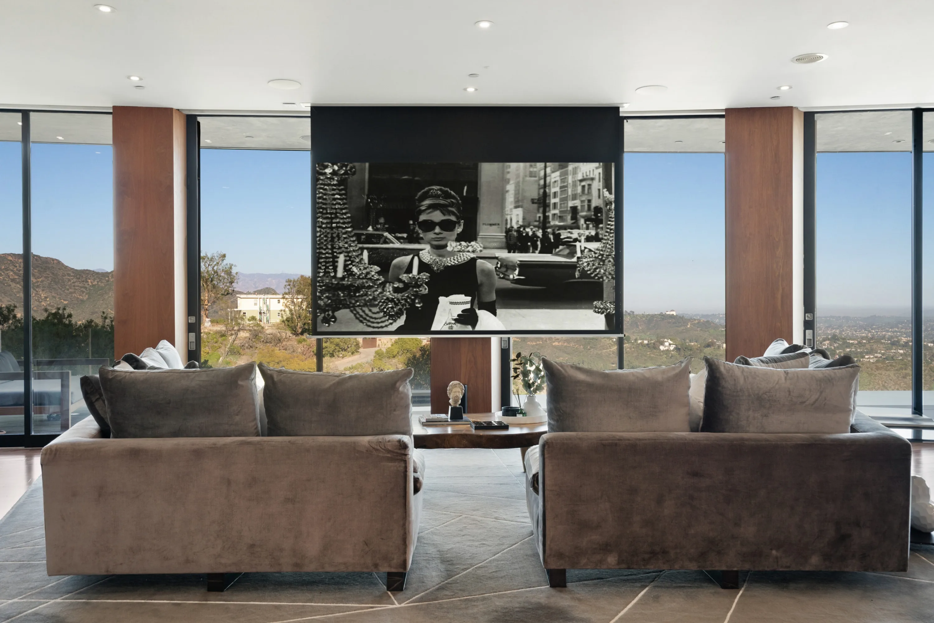 Media lounge with drop-down projector screen showing a black-and-white film, hills visible either side