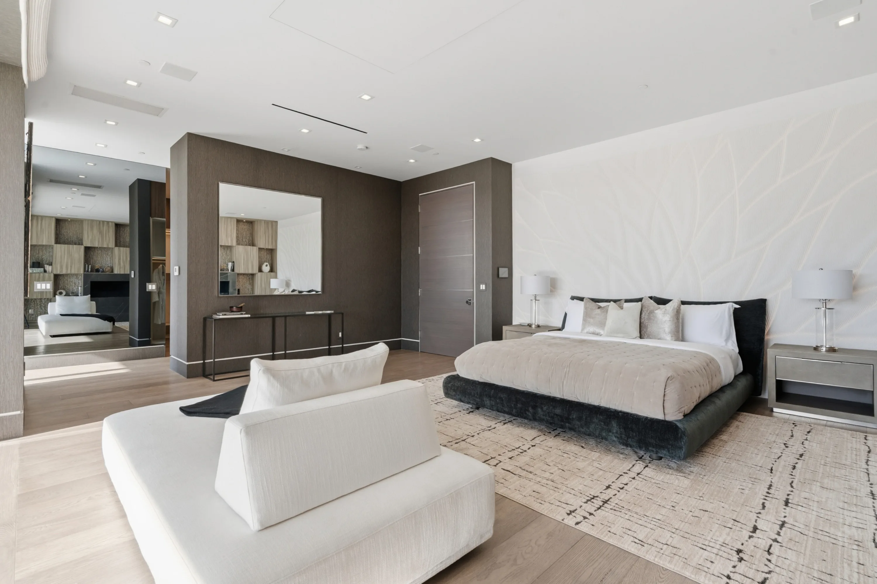 Guest bedroom with charcoal upholstered bed, etched feature wall and a lounge area leading to the dressing room