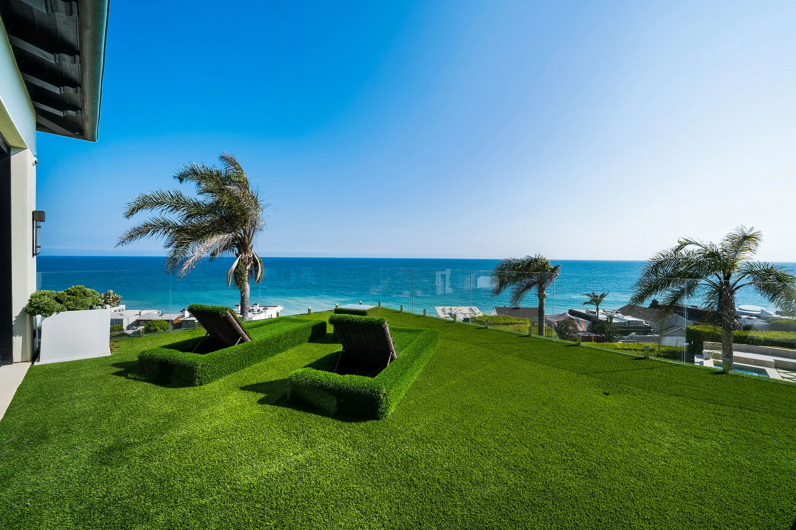 Clifftop lawn terrace with two turf-clad sun loungers, glass railing and turquoise water below