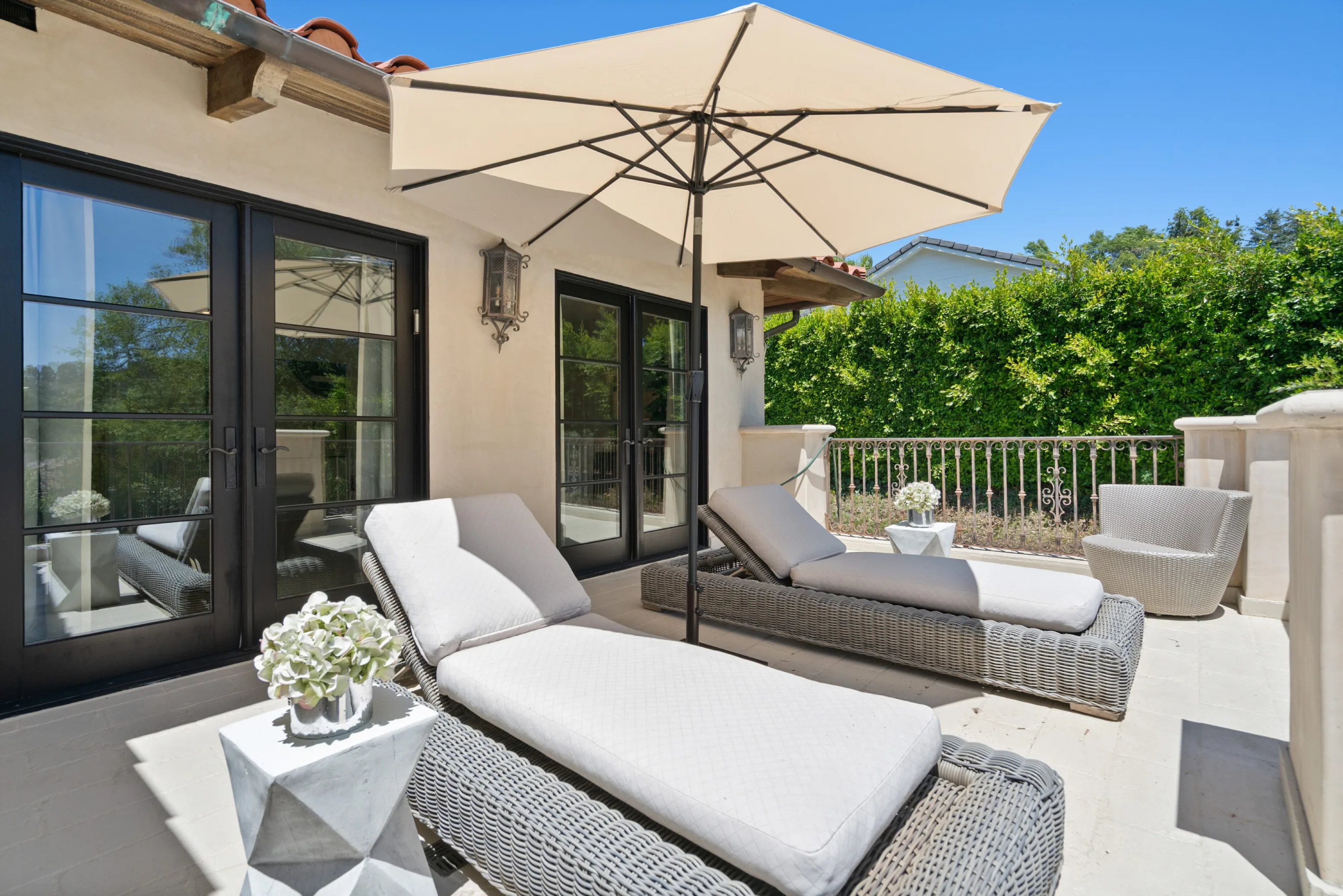 Upper terrace lined with woven chaises and a parasol outside black-framed French doors