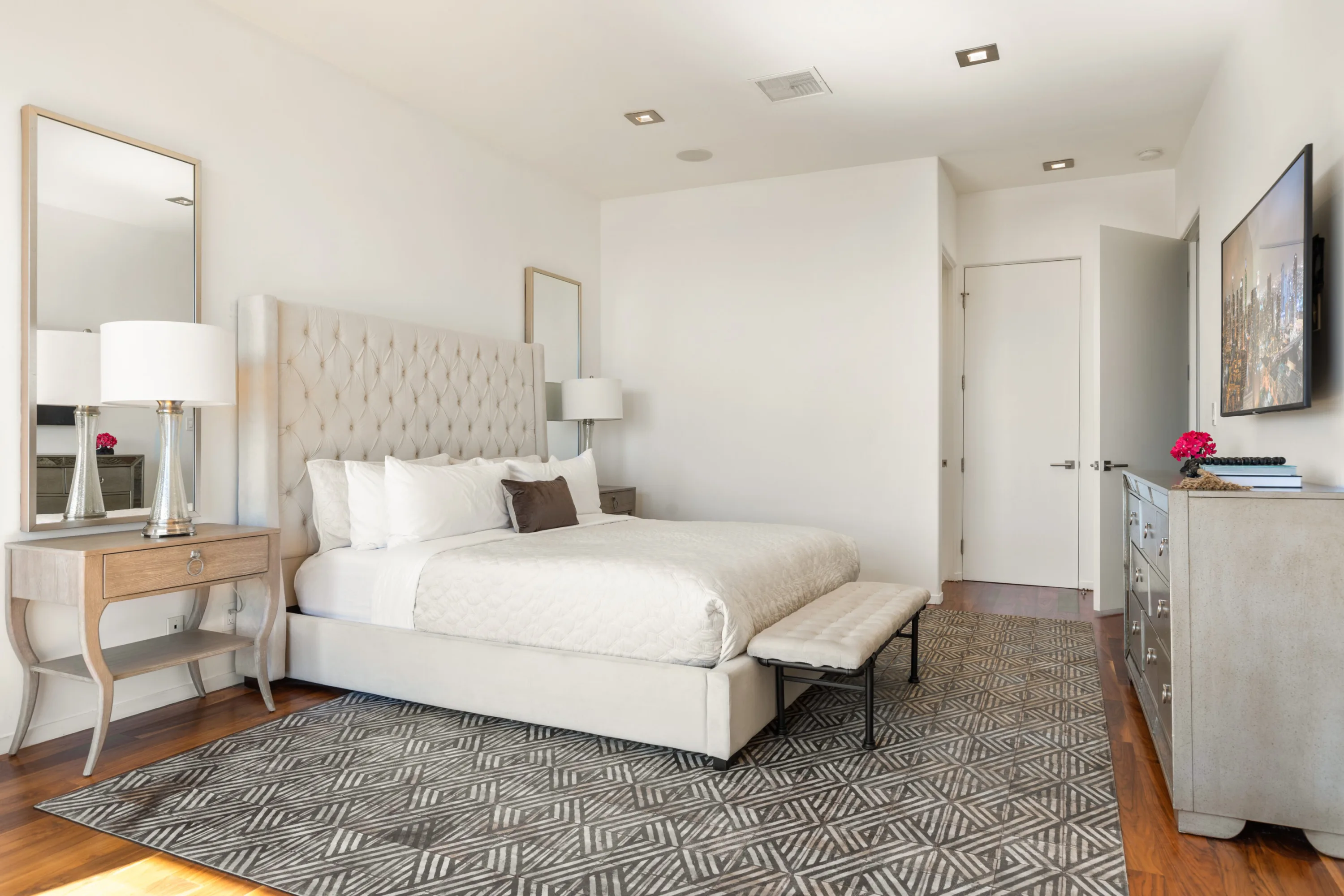 Guest room with diamond-tufted headboard, upholstered bench and patterned rug on walnut floors