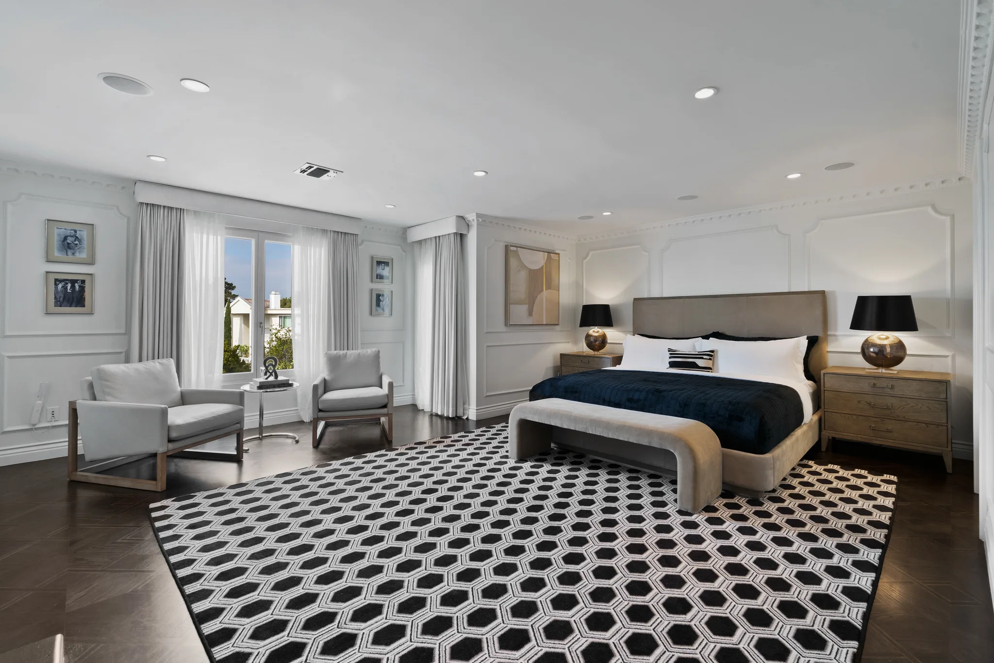 Spacious bedroom suite with navy-throw king bed, bold hexagon-patterned rug and two armchairs in the window nook