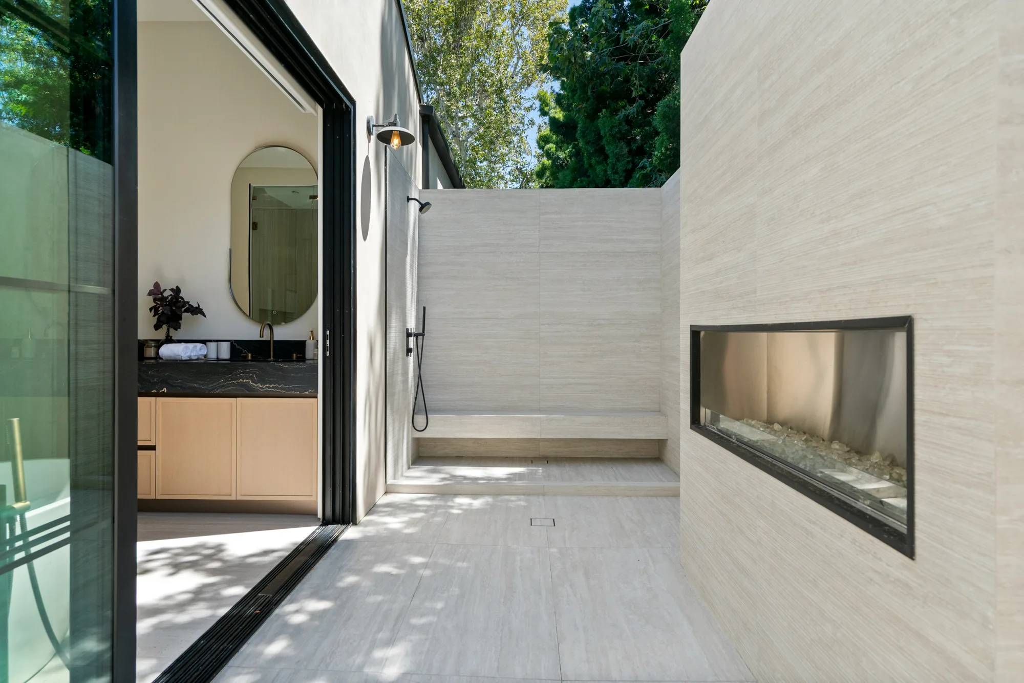 Walled outdoor shower off the primary bath, with bench seating and a linear fire feature