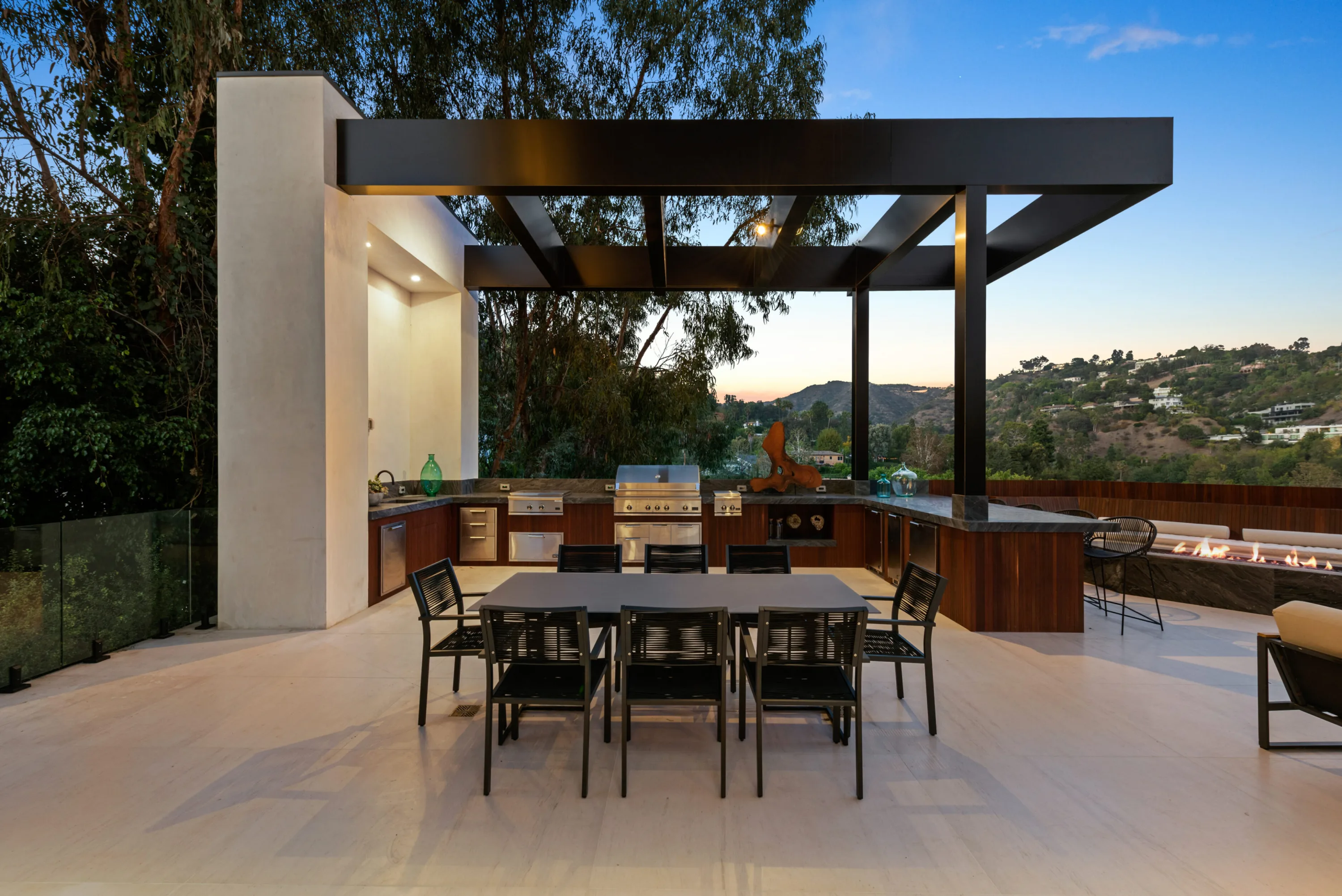 Covered outdoor kitchen and dining terrace with built-in grill, linear fire feature and canyon at sunset