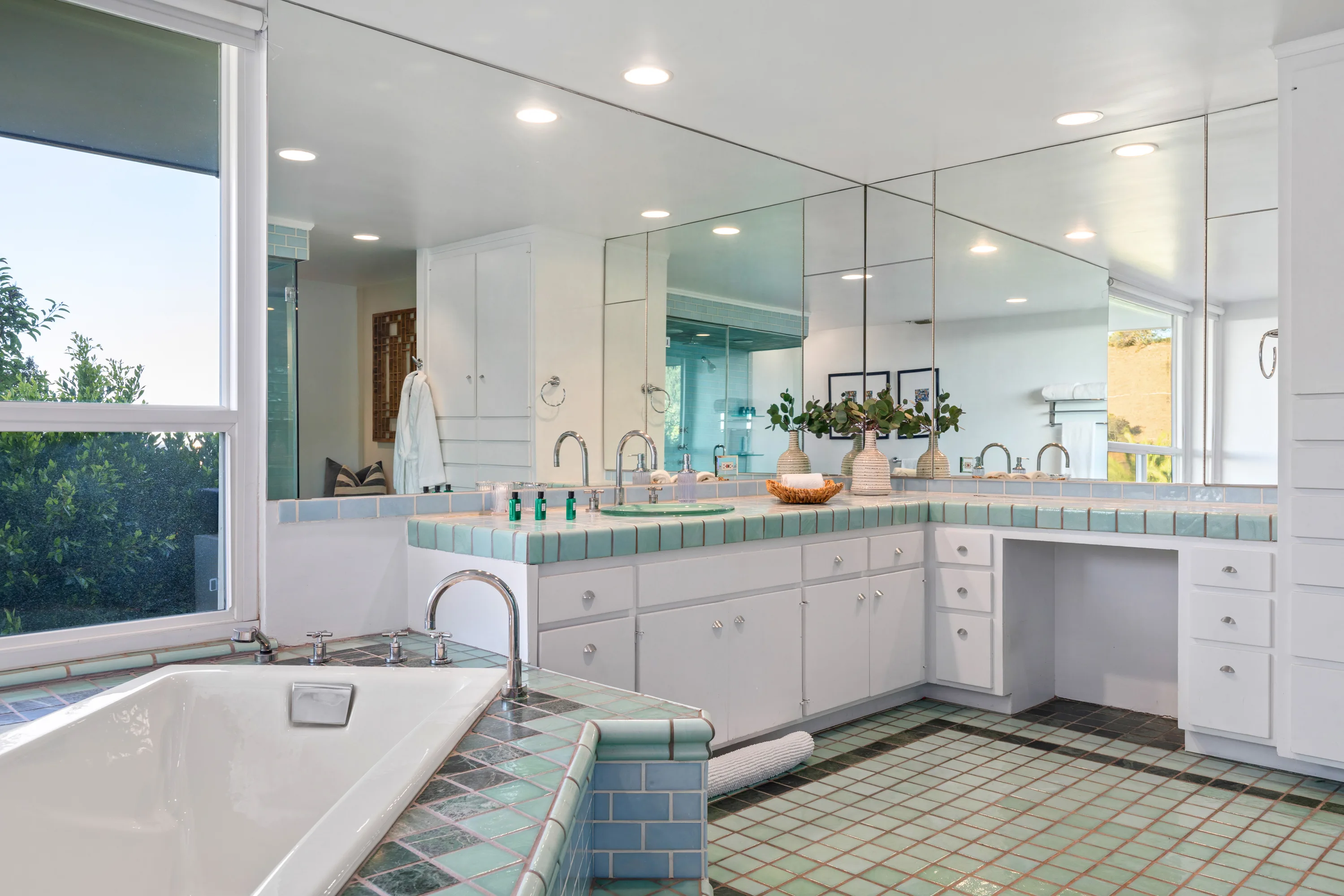Primary bath with mint-tiled double vanity, vanity desk and soaking tub set below a garden window