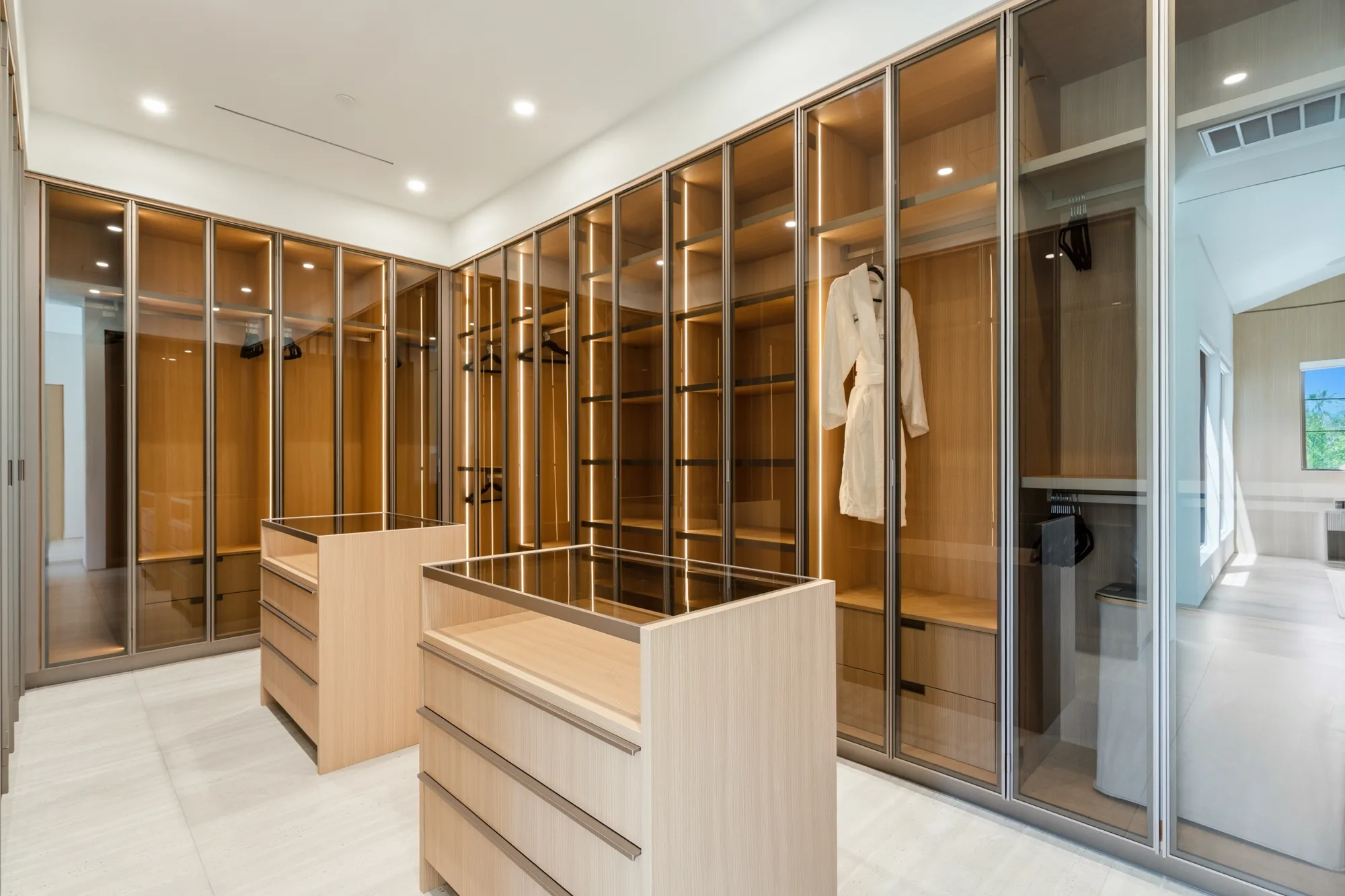 Walk-in dressing room with backlit glass-fronted oak wardrobes, island drawers and a waiting robe