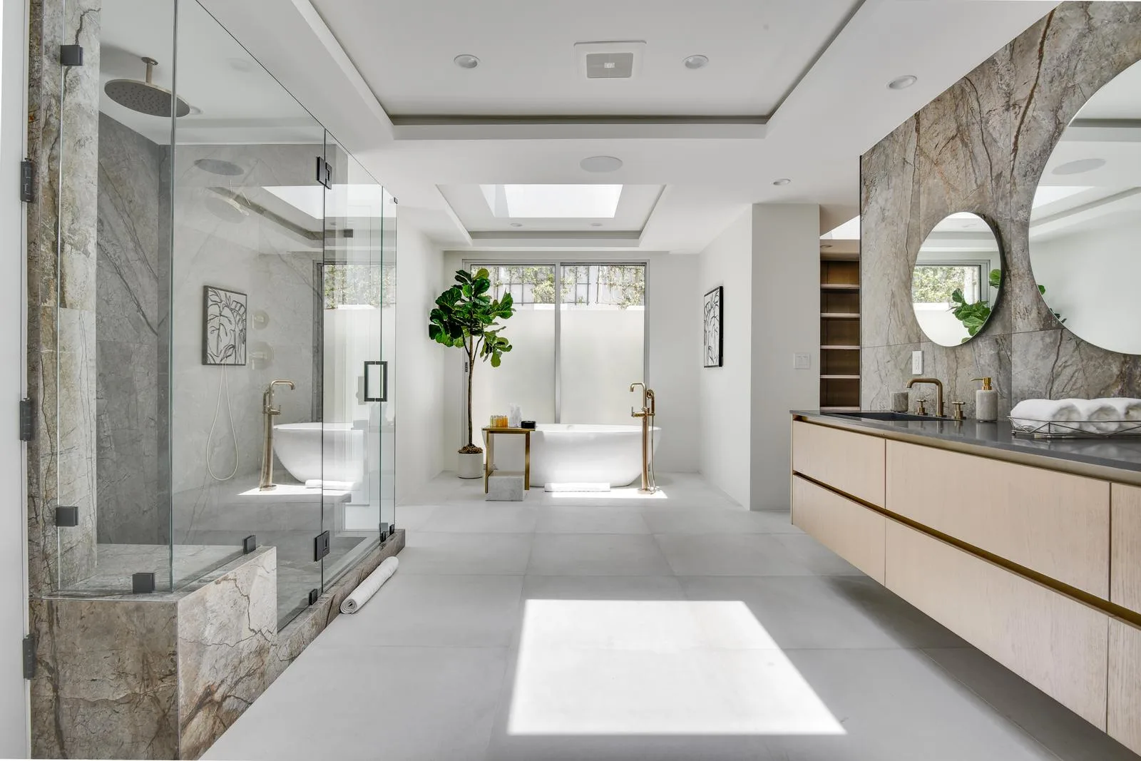 Primary suite bathroom with walk-in stone shower, freestanding tub beneath a skylight and floating double vanity