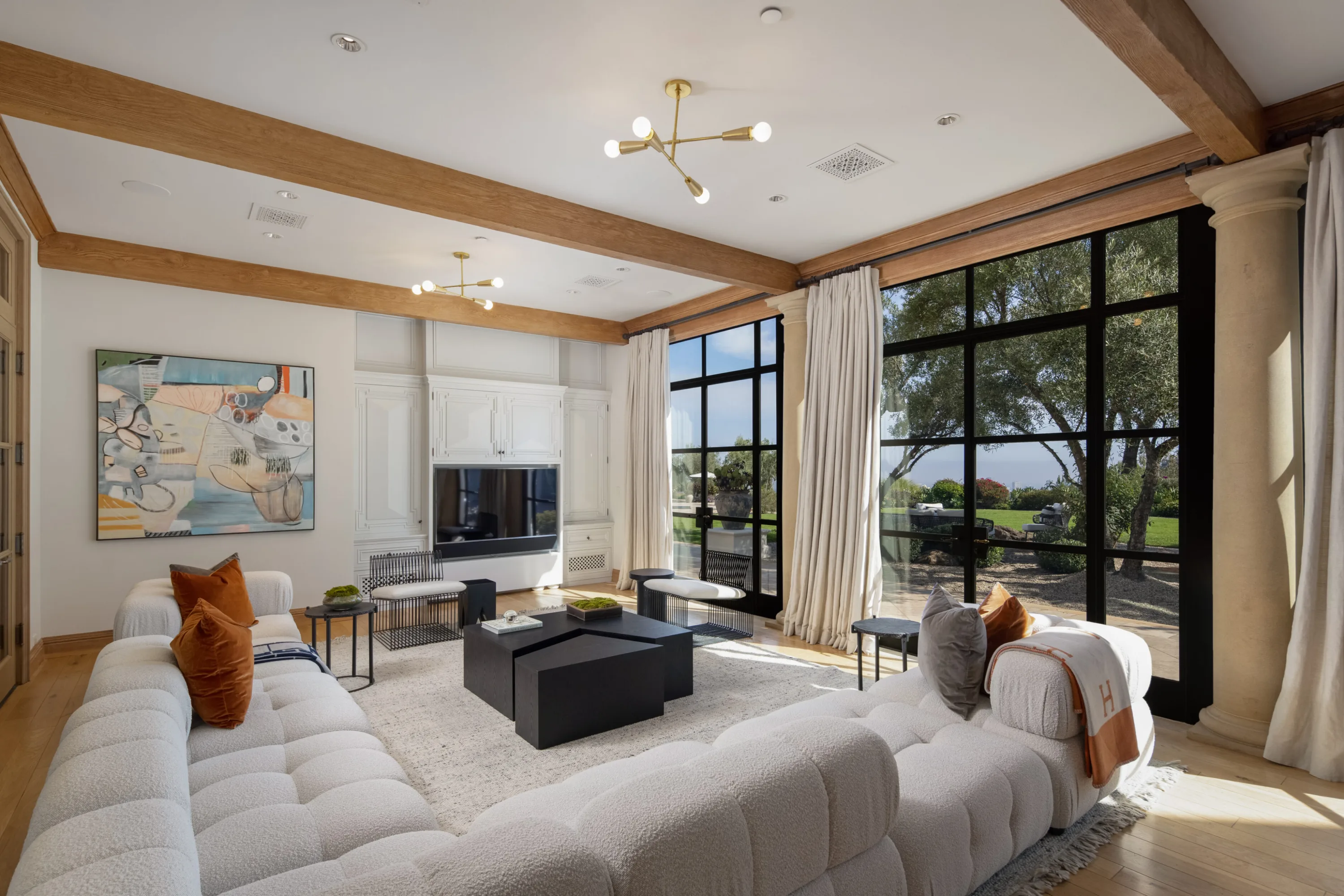 Family room with deep bouclé sectionals, media wall and full-height steel windows onto the lawn
