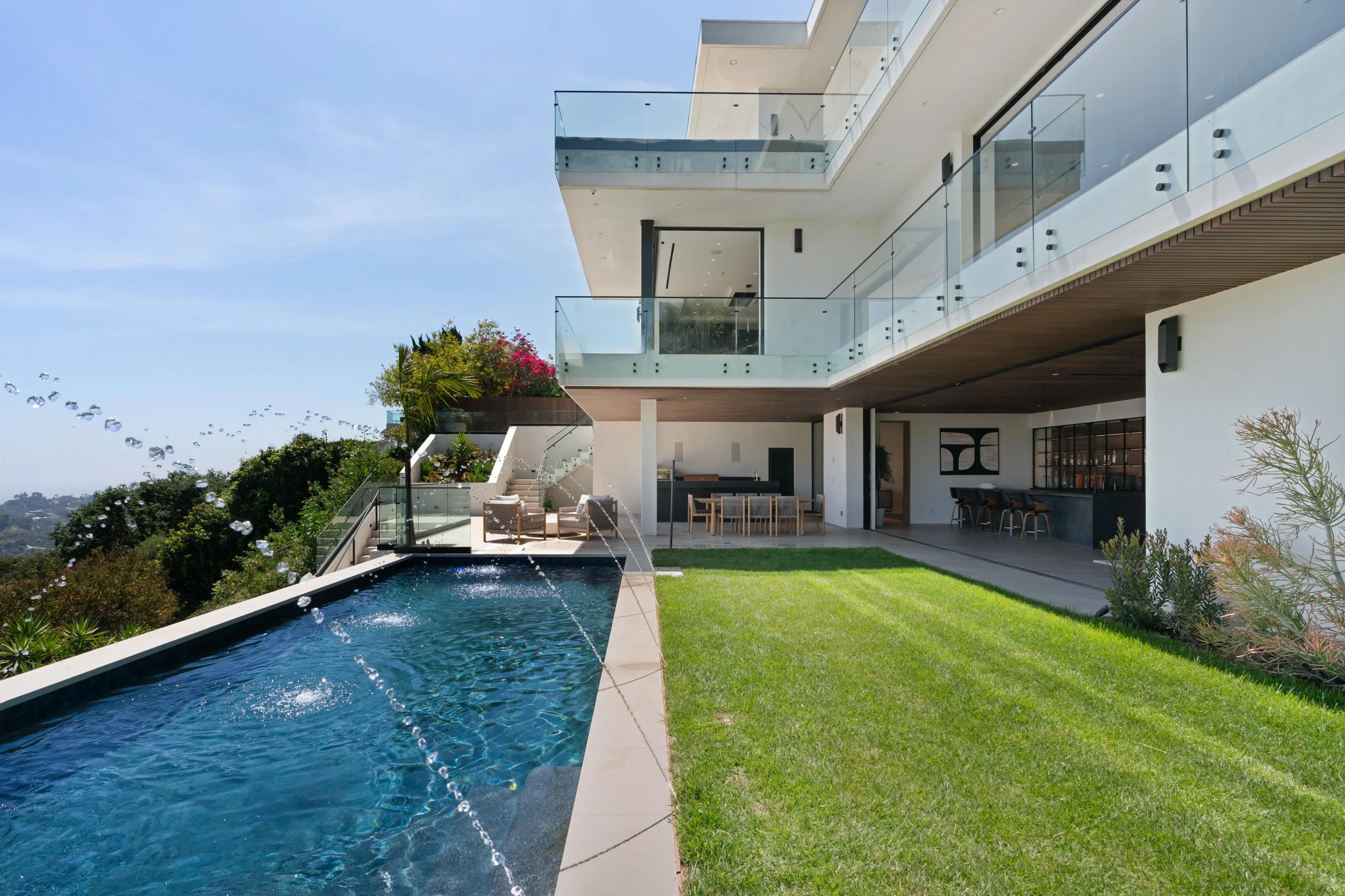 Rear elevation of the Bel Air estate with lap pool, striped lawn and glass-railed terraces above the canyon