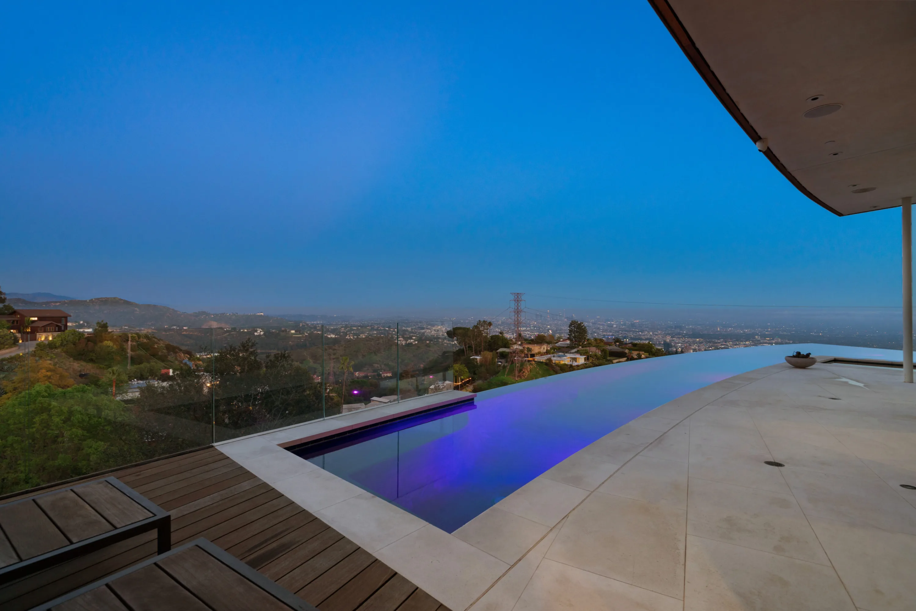 Infinity pool glowing violet at blue hour above the canyon, with city lights stretching to the horizon