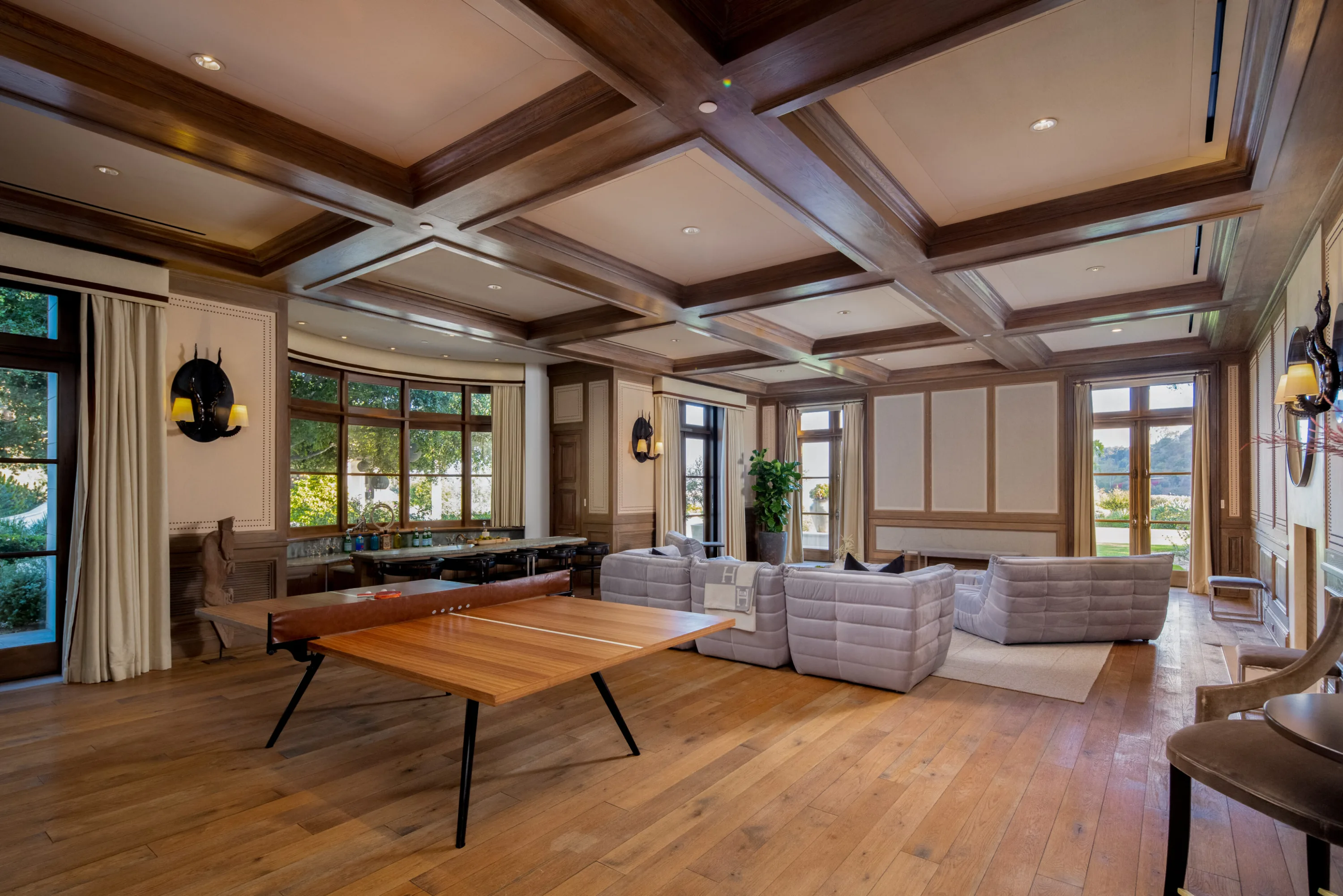 Games lounge with ping-pong table, low modular sofas and coffered wood ceiling under bay windows