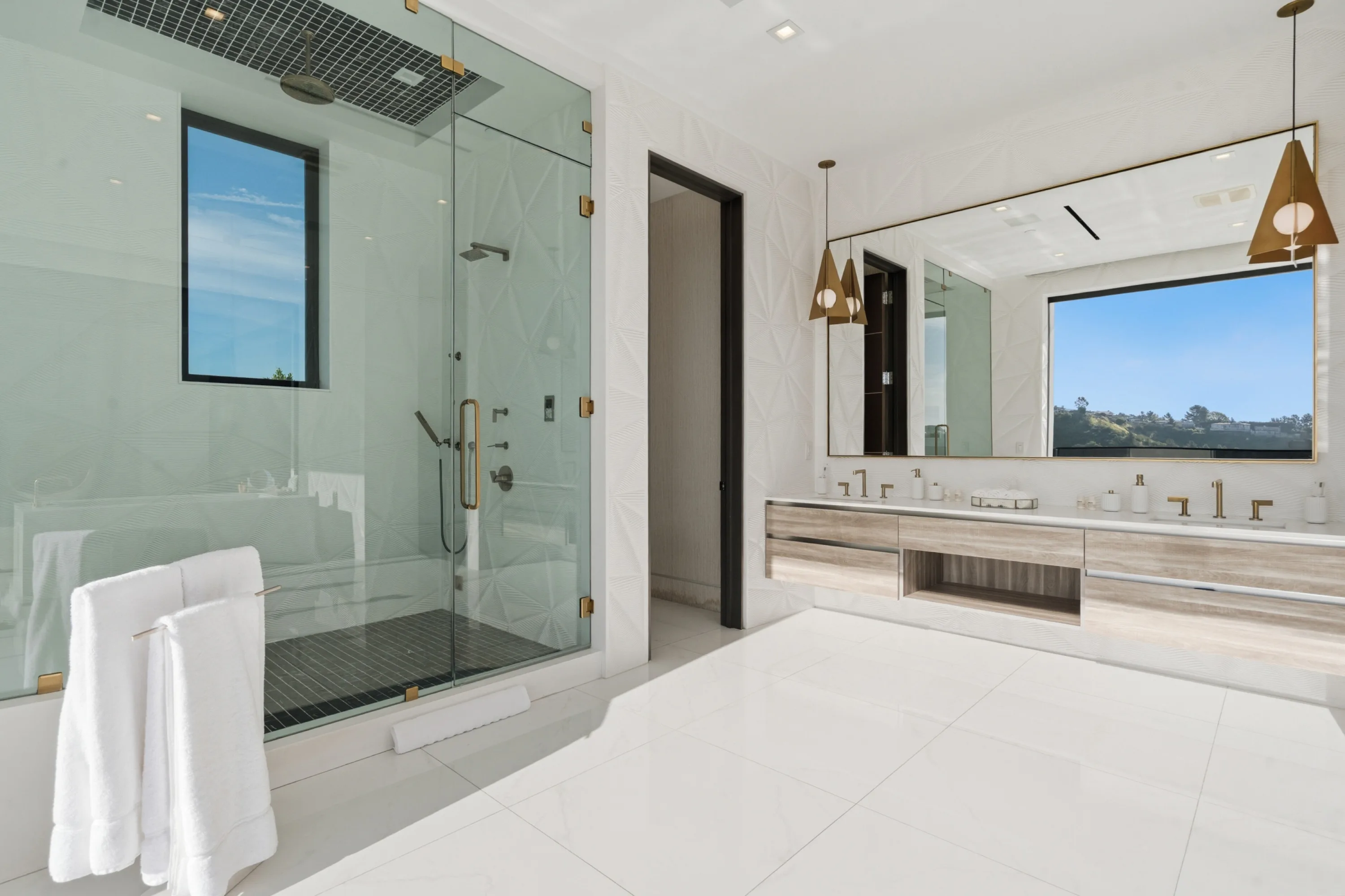 Primary bathroom with walk-in steam shower, double floating vanity and brass pendants framing a hillside window