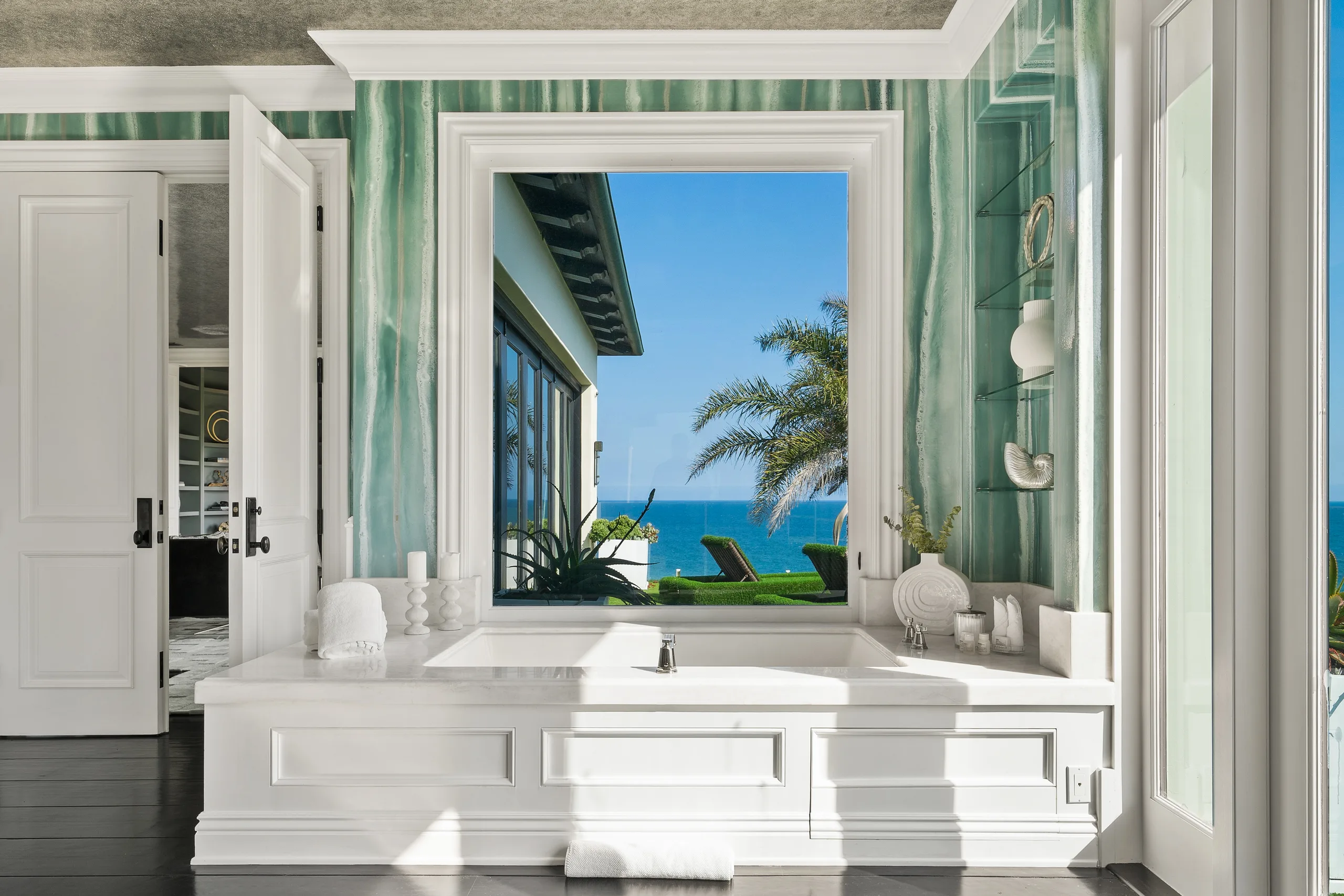Primary bath soaking tub set beneath a picture window onto palms and open ocean, green agate walls