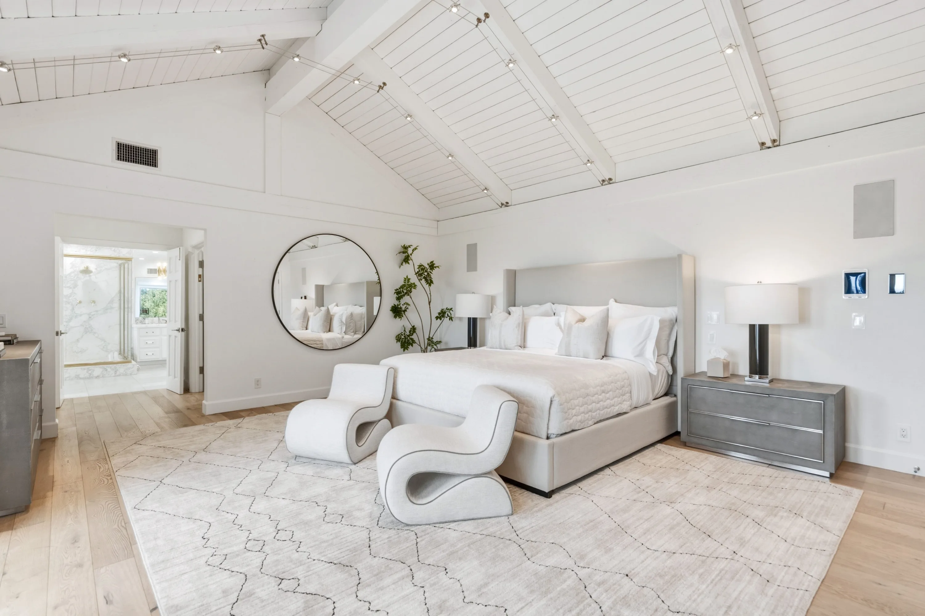 Primary bedroom from the window side, round mirror and open doorway to the marble ensuite bath
