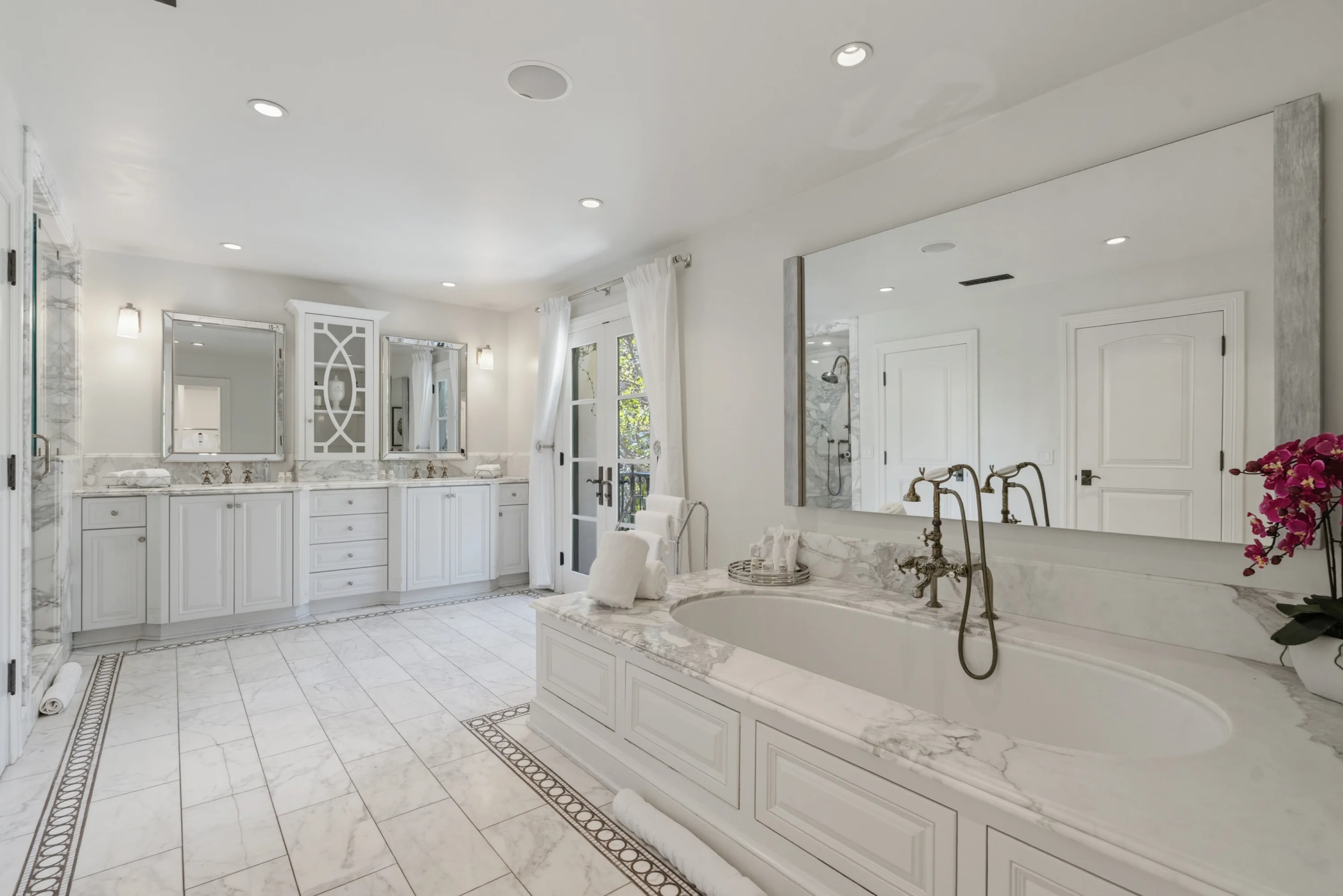 Marble primary bathroom with double vanities, soaking tub set in stone and an oversized mirror