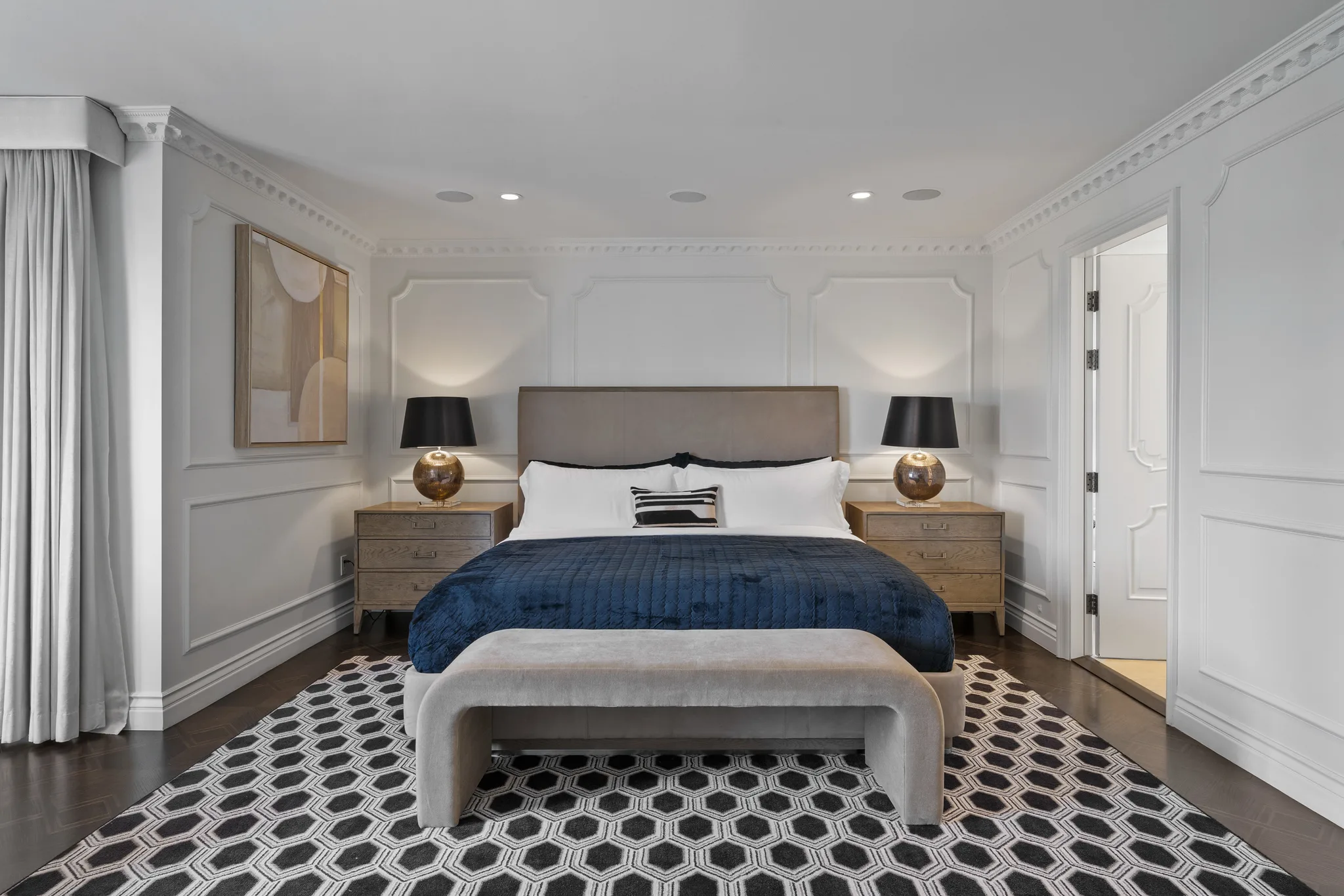 Symmetrical view of the same bedroom: velvet headboard between brass lamps, oak nightstands and a curved suede bench