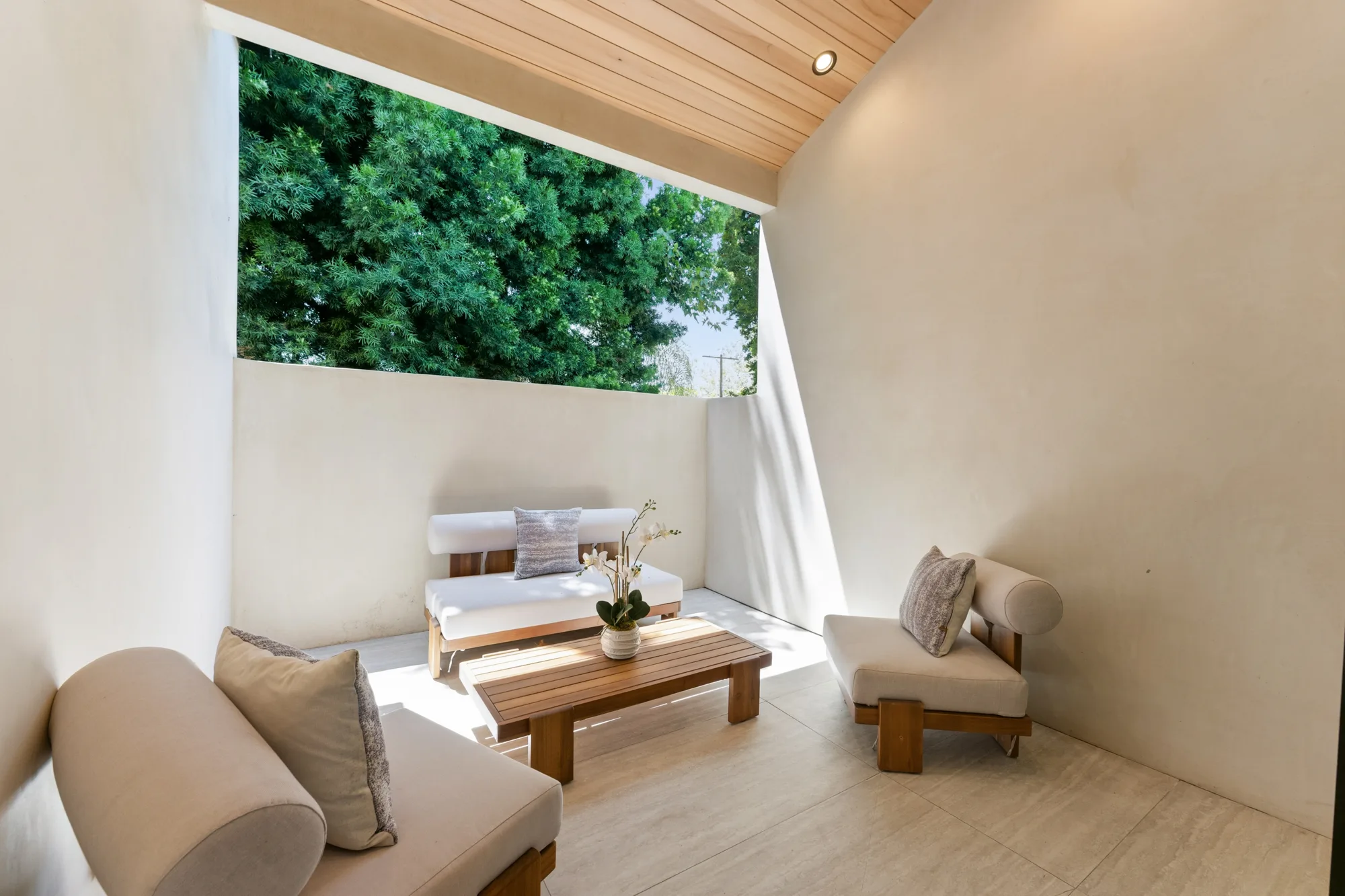Sheltered side courtyard with teak-framed daybeds, low slatted coffee table and an open wall framing treetops