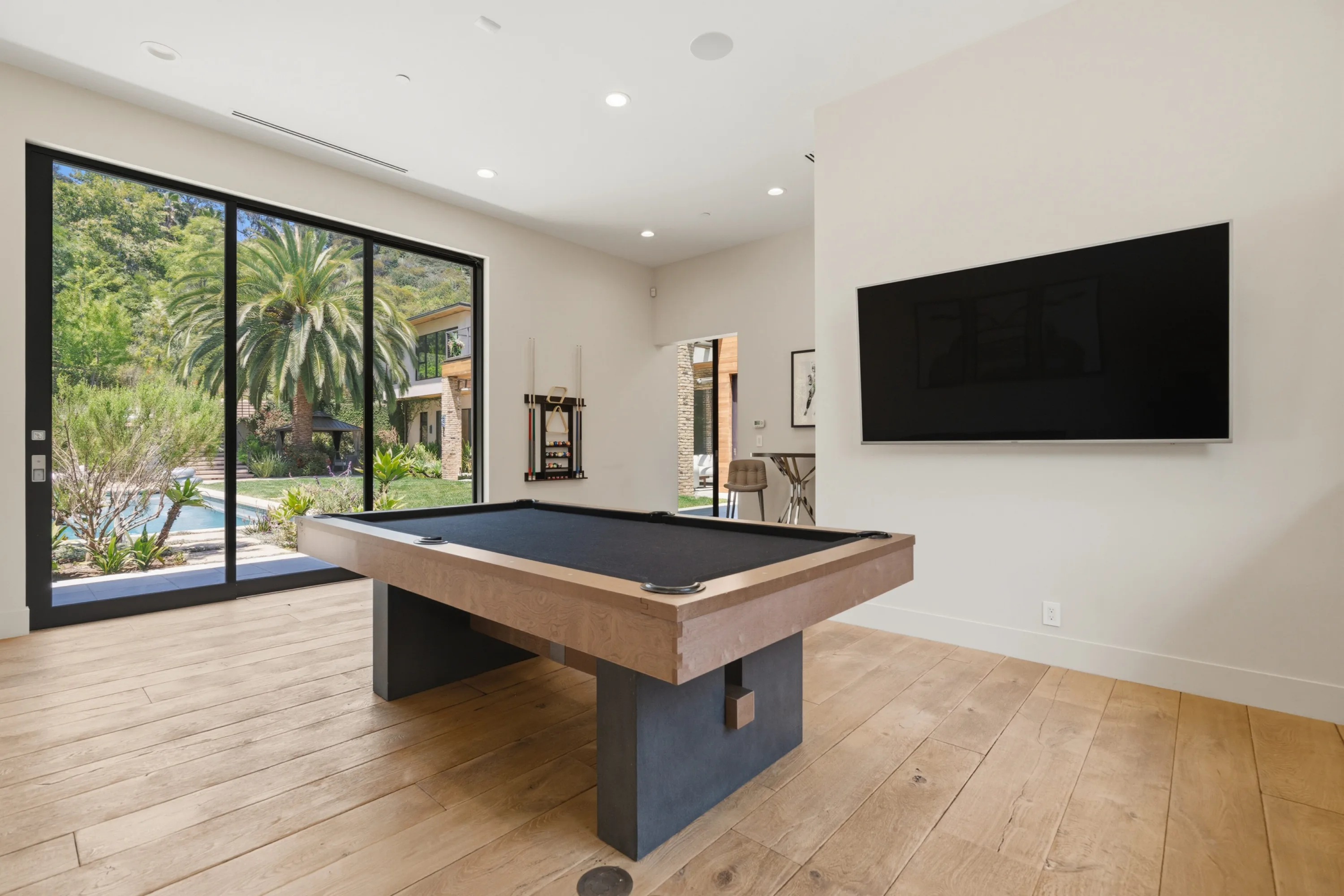 Games room with pool table and wall-mounted TV, glass doors opening onto palms and the pool deck