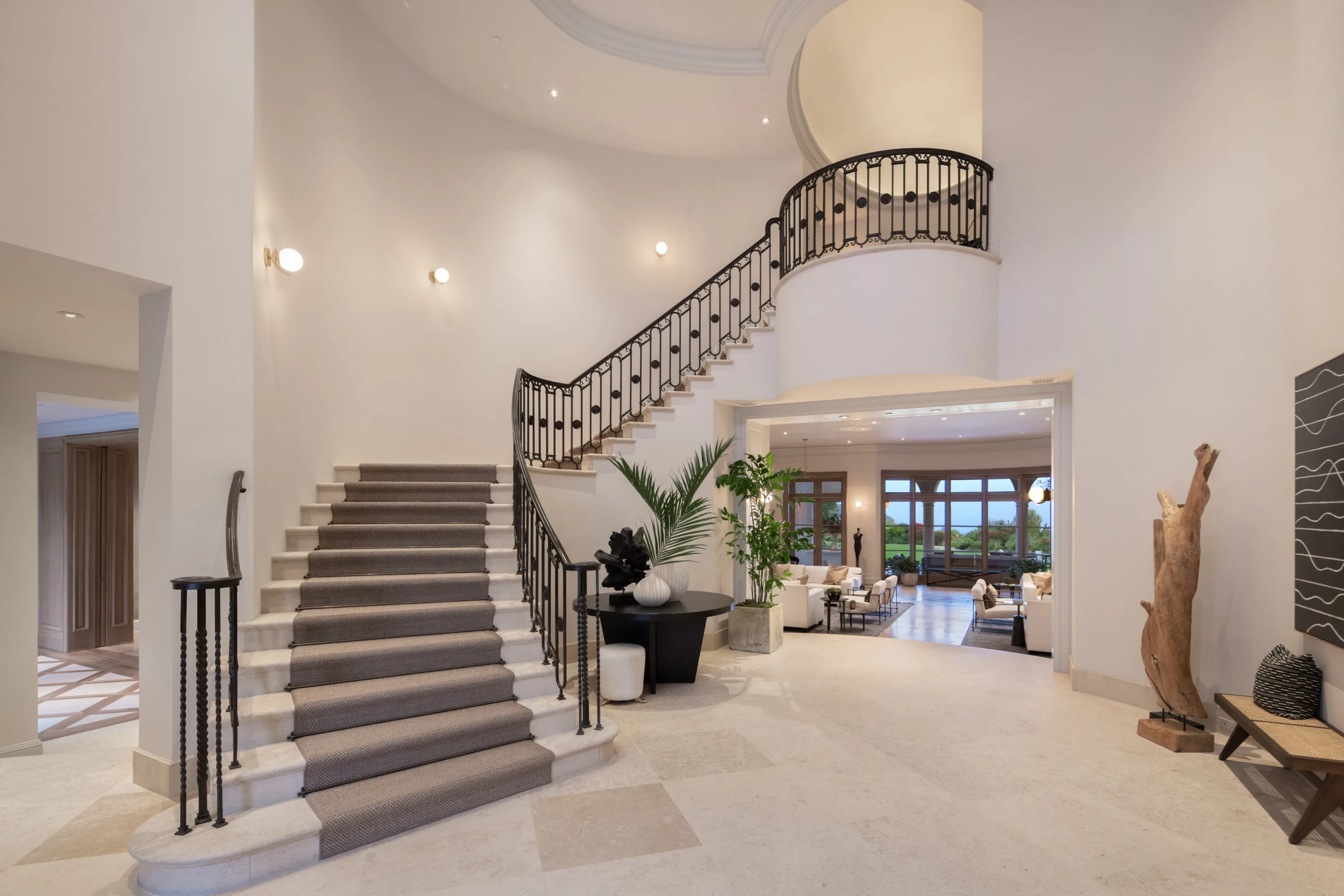 Double-height entry hall with curved wrought-iron staircase opening to the living room beyond