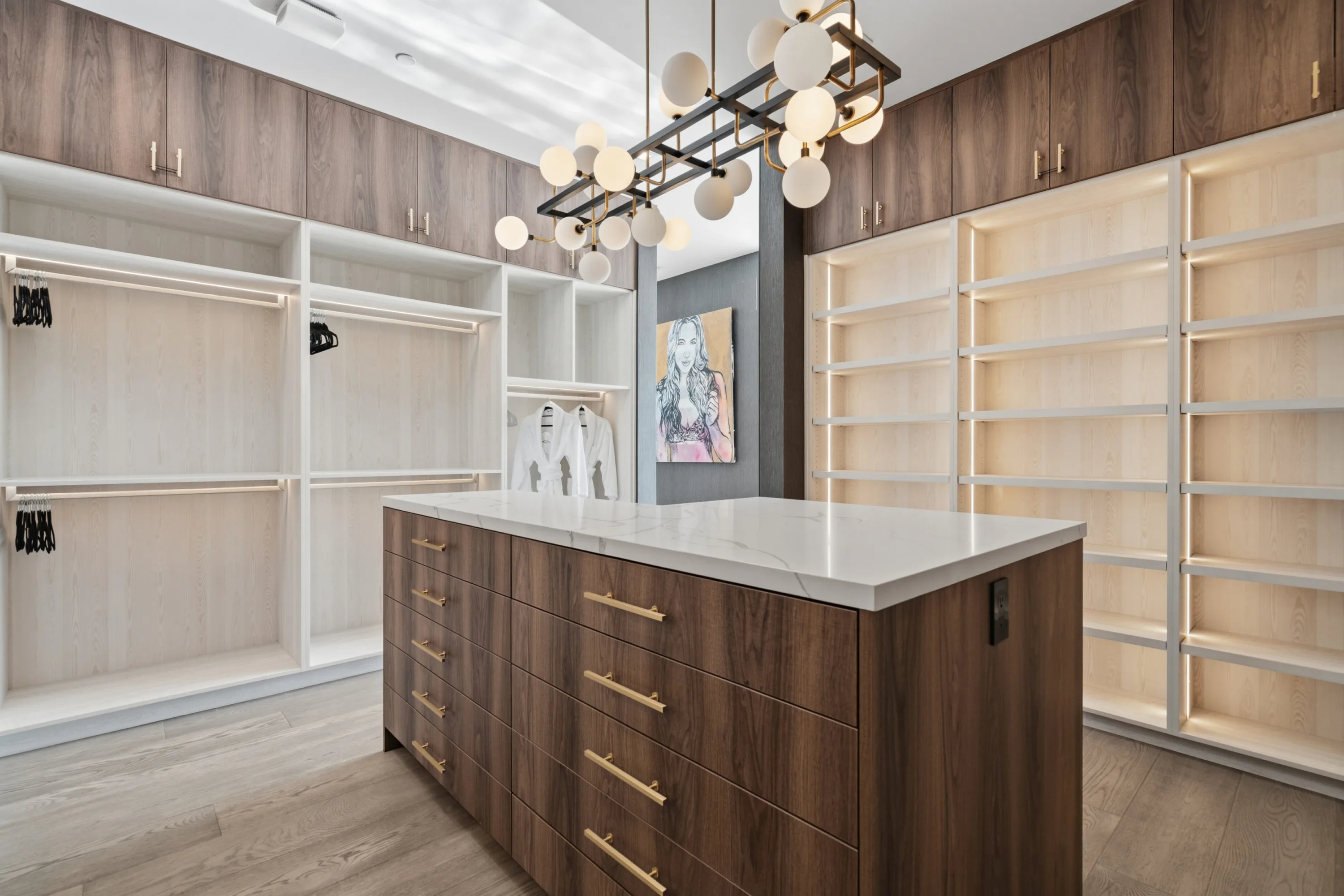 Walk-in dressing room with lit shelving, walnut island and a sculptural globe chandelier overhead
