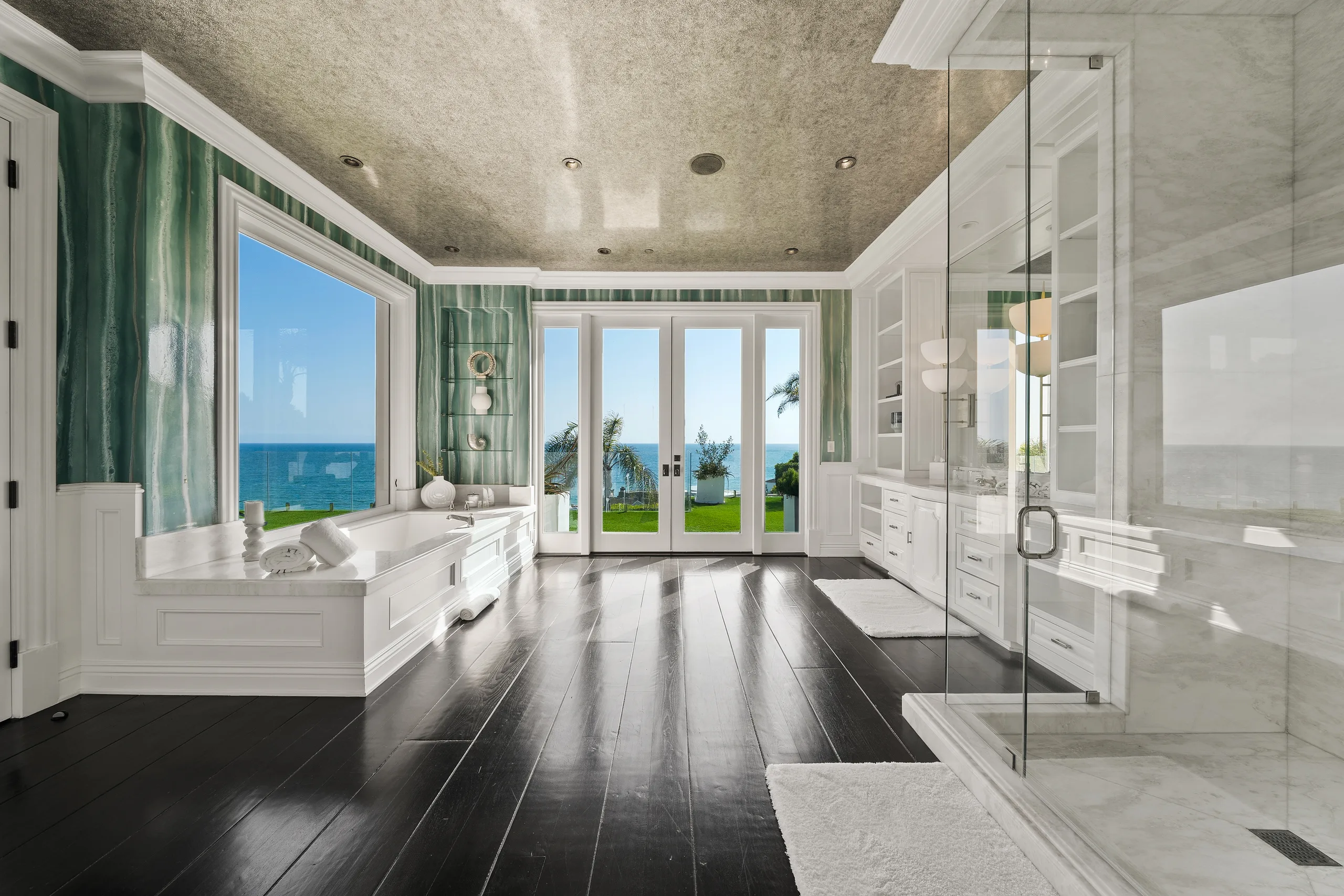 Primary bath with soaking tub set beneath a picture window framing the Pacific, green onyx walls and marble shower