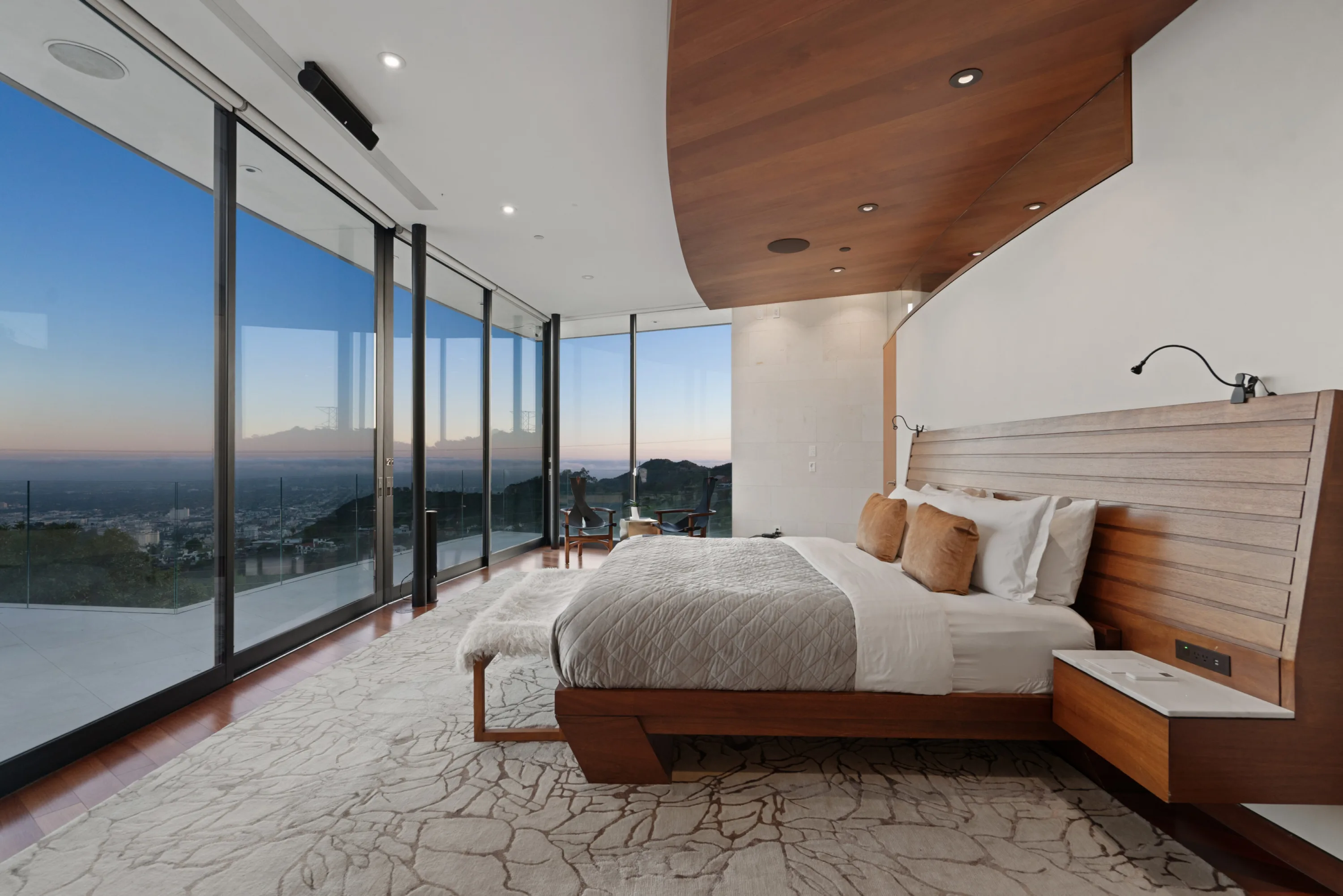 Primary suite at dawn, timber platform bed and headboard, curved wood ceiling and glass to the terrace