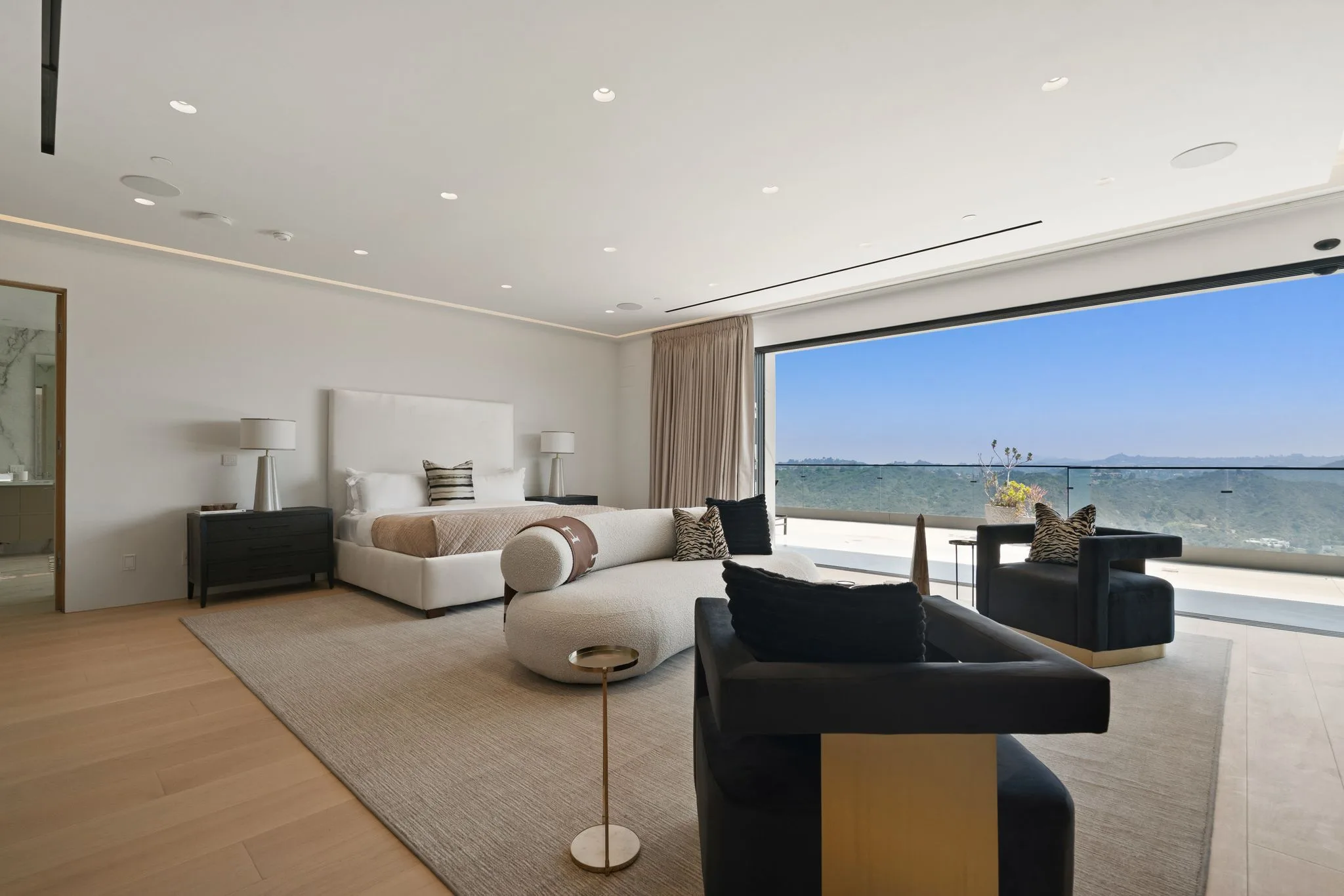 Wide angle of the primary bedroom's seating area and bed, framed by the full-height view window