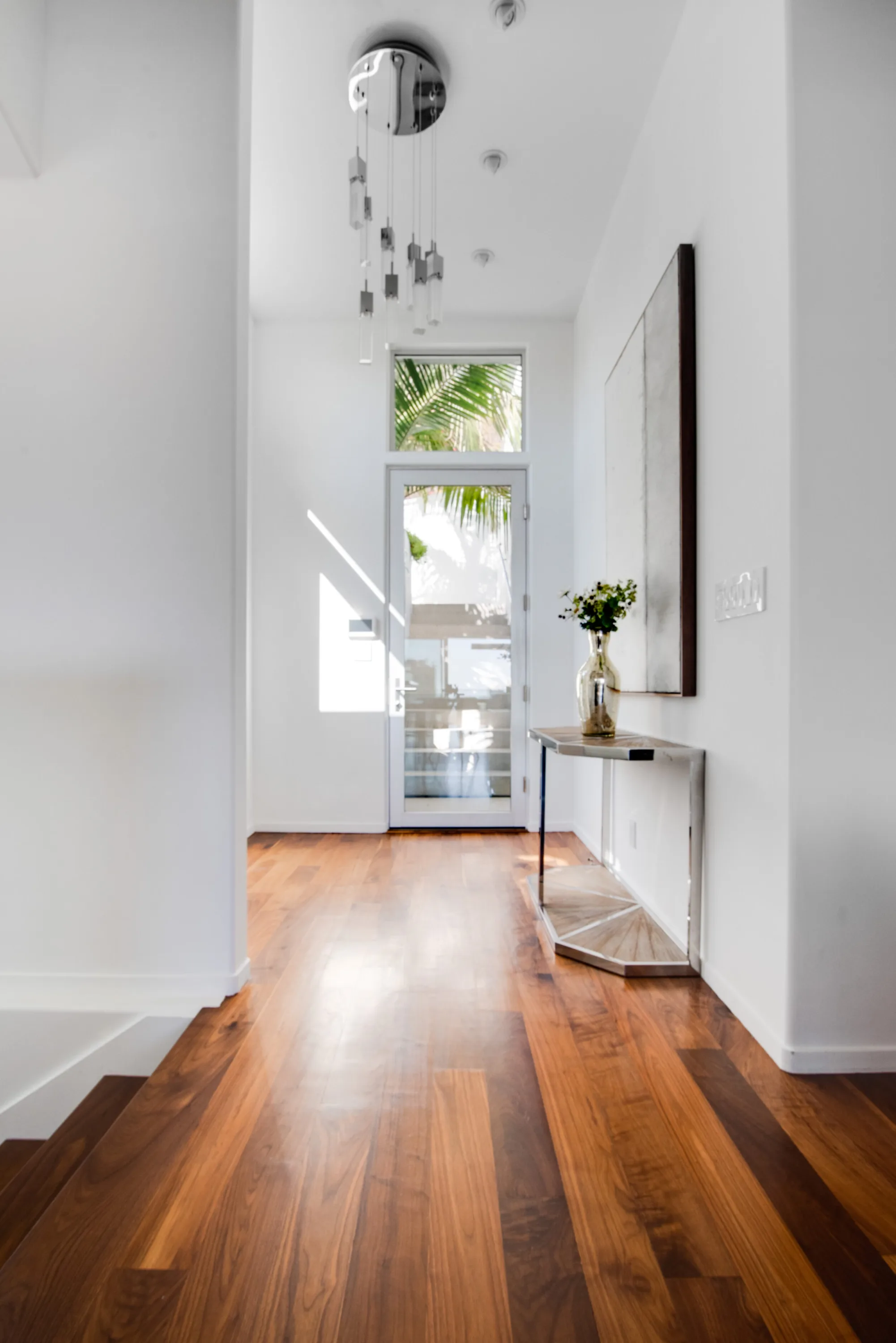 Entry hall in walnut plank flooring leading to the glass front door under a cascading pendant light