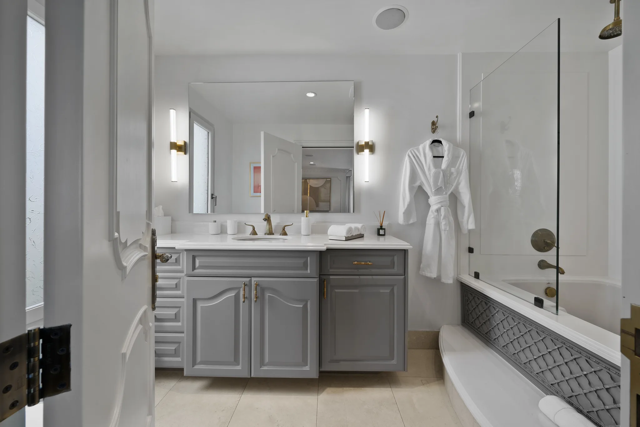 Guest bathroom with grey double-door vanity, brass fixtures, waiting robe and a glass-screened tub with rain head