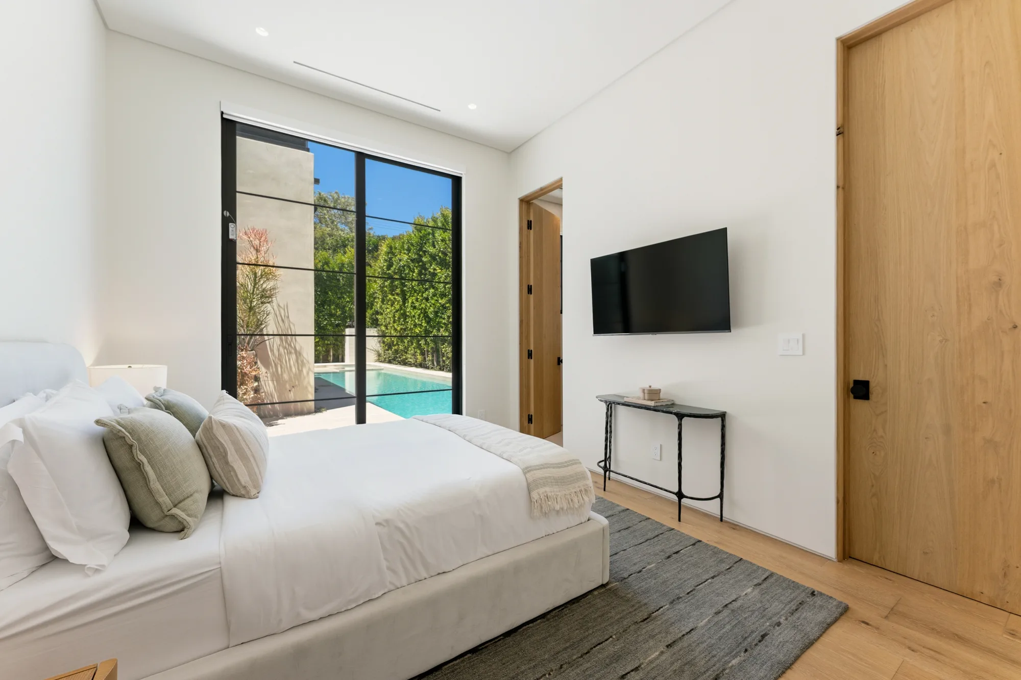 Poolside guest bedroom where sliding glass doors open straight onto the water, wall-mounted TV opposite the bed