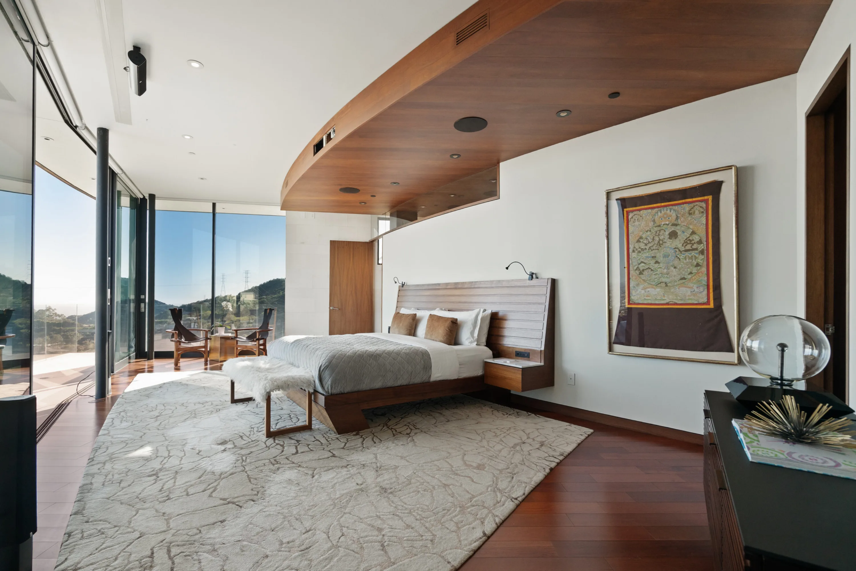 Primary bedroom by day, framed textile artwork, sheepskin bench and sliding doors to a sunlit terrace