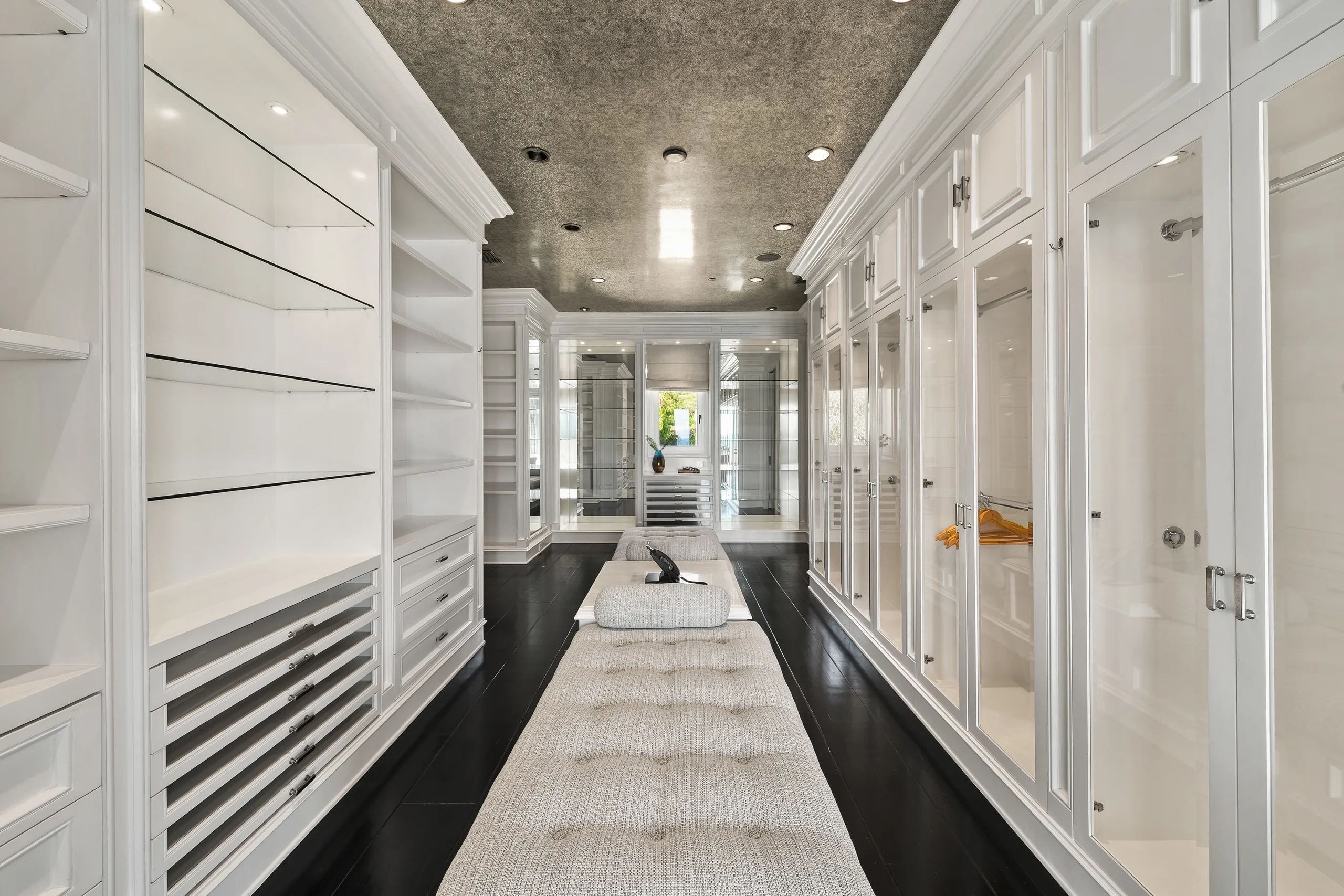 Walk-through dressing room lined with glass-front wardrobes and a long tufted bench down the centre