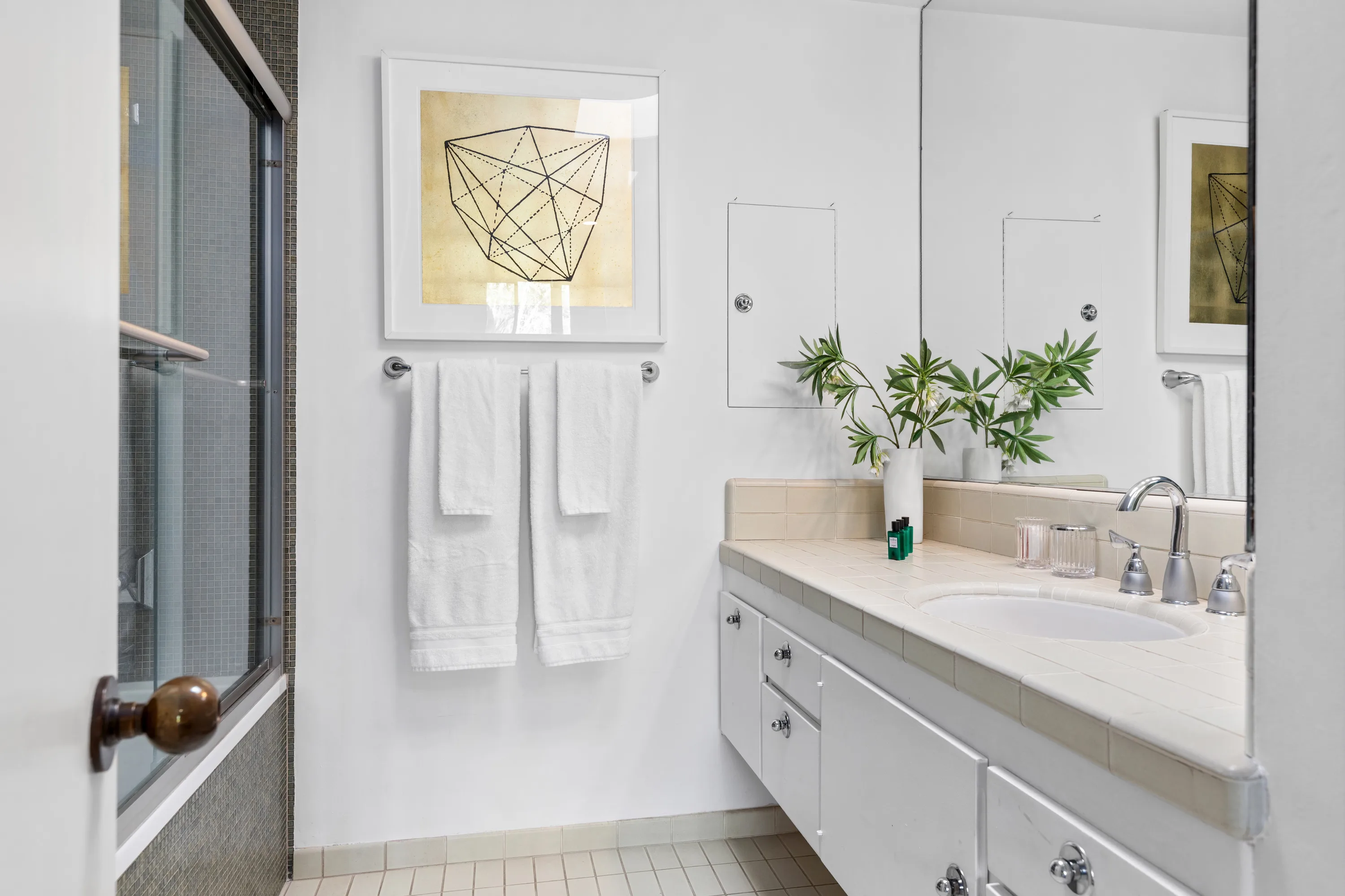 Crisp guest bathroom with tiled vanity, framed geometric print and shower-over-tub