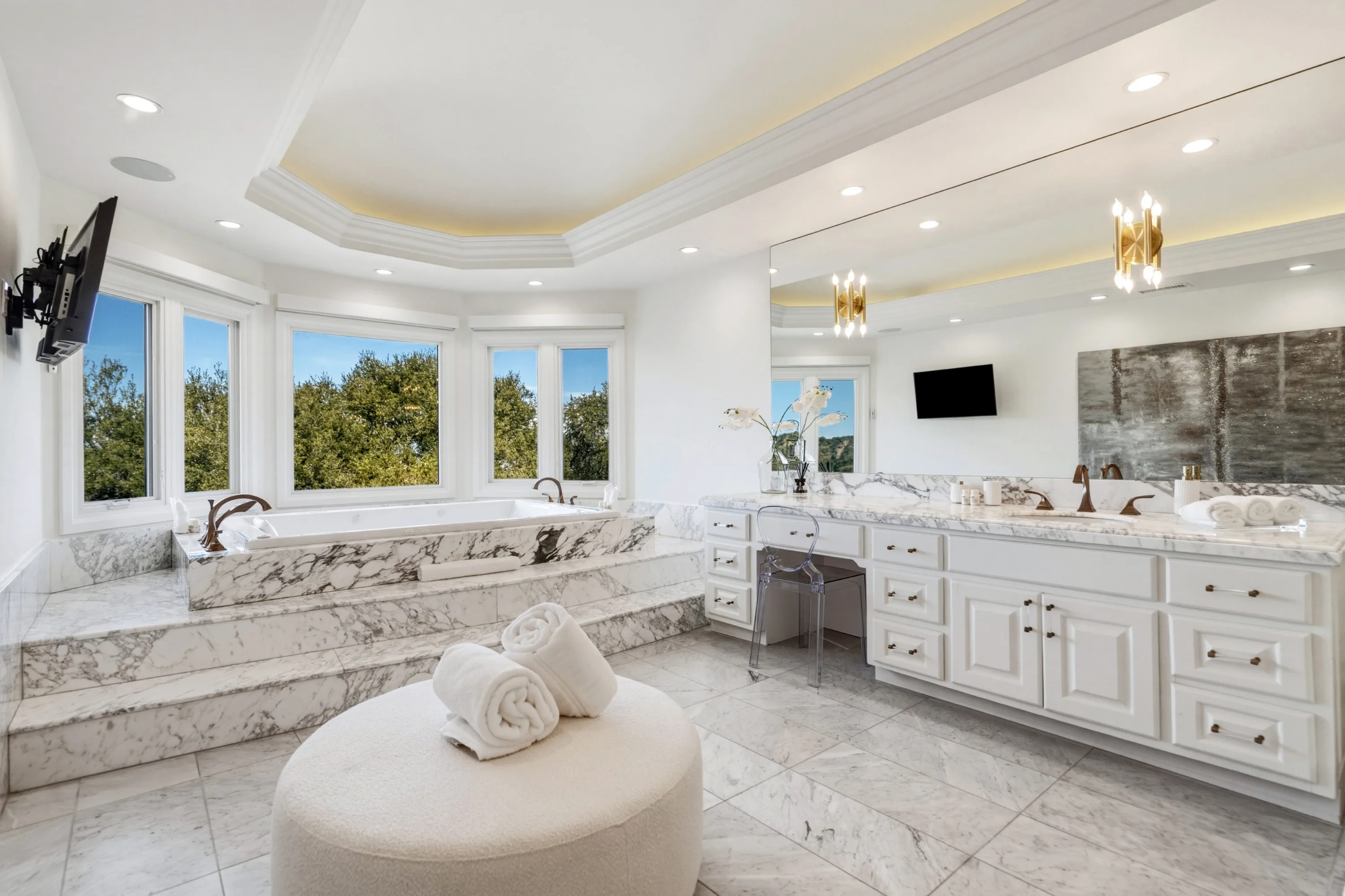 Marble primary bath with raised soaking tub under bay windows, twin vanities and vanity desk