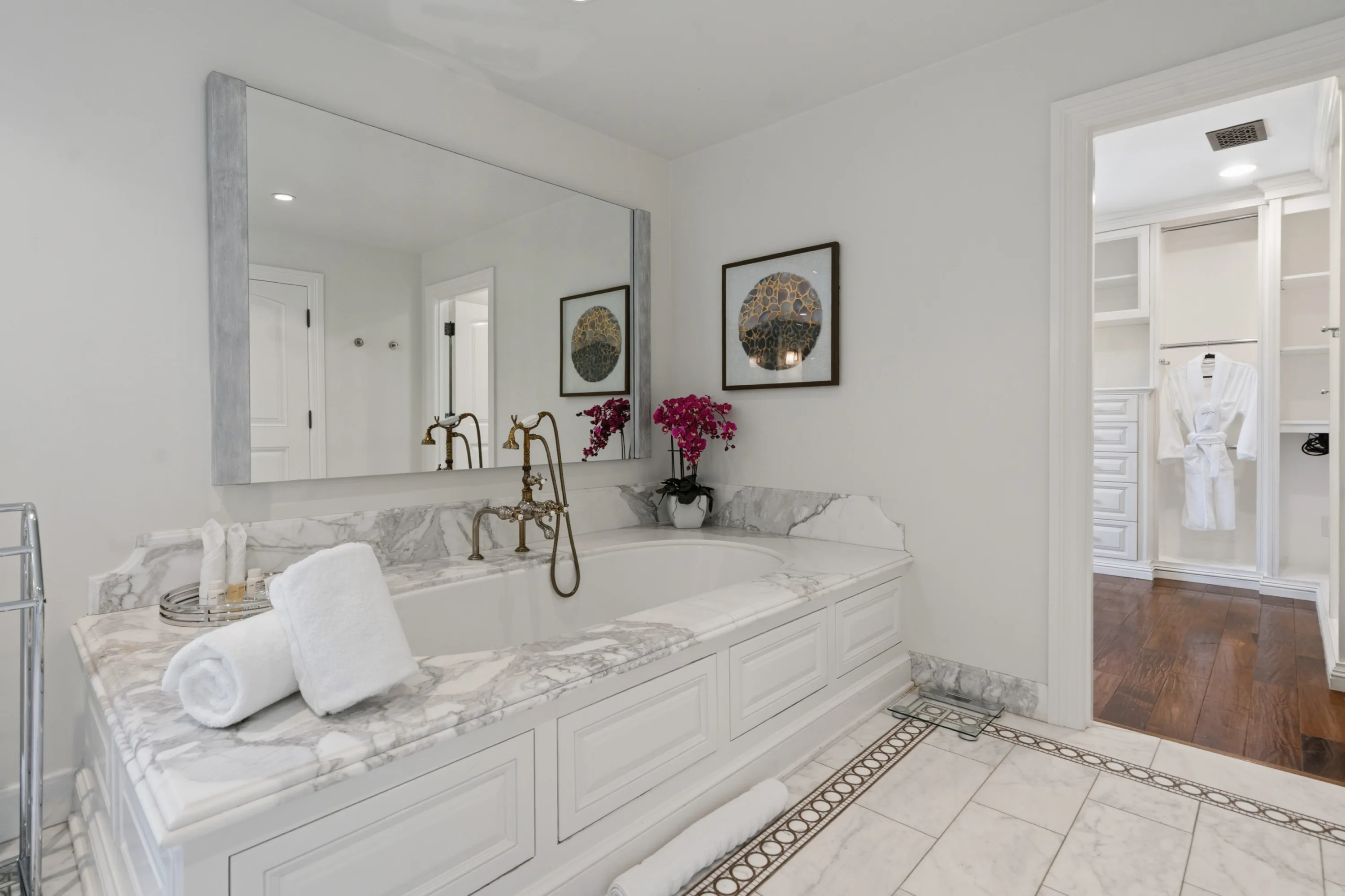 Soaking tub with aged brass fittings and orchids, rolled towels and dressing room glimpsed beyond