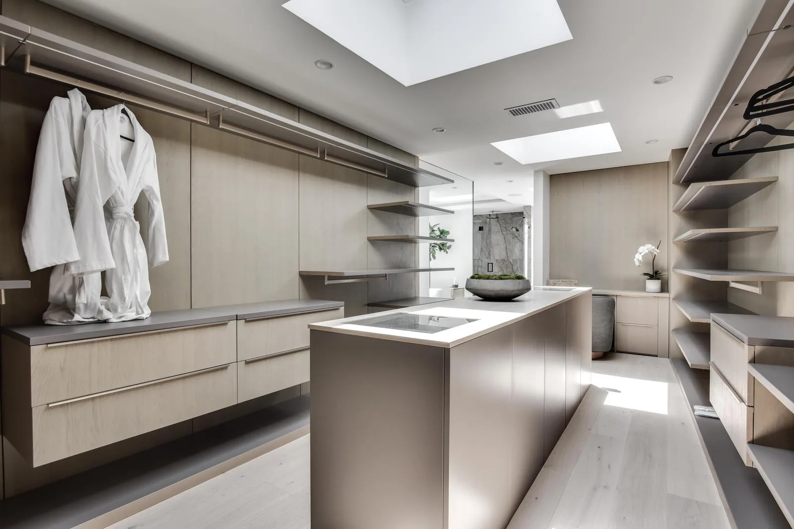 Walk-in dressing room with island, open shelving, skylights and two white robes hanging ready