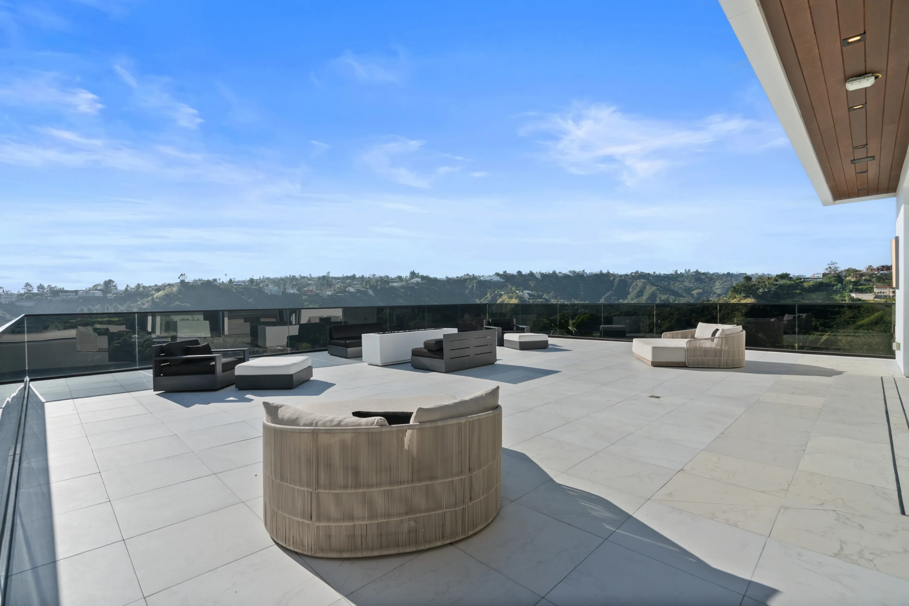 Vast stone-paved upper terrace with woven lounge seating and glass railings open to canyon and hillside views