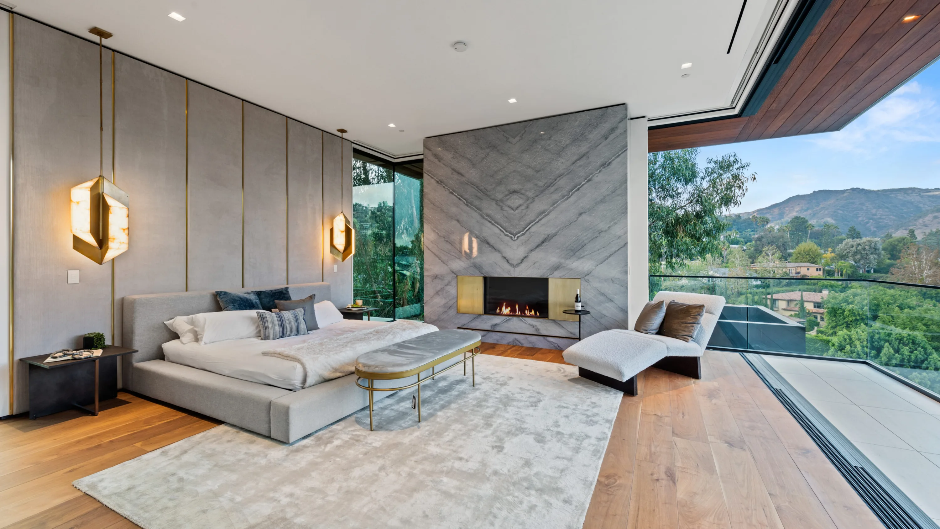 Primary suite with marble fireplace, chaise by the glass wall and mountain views from the corner opening