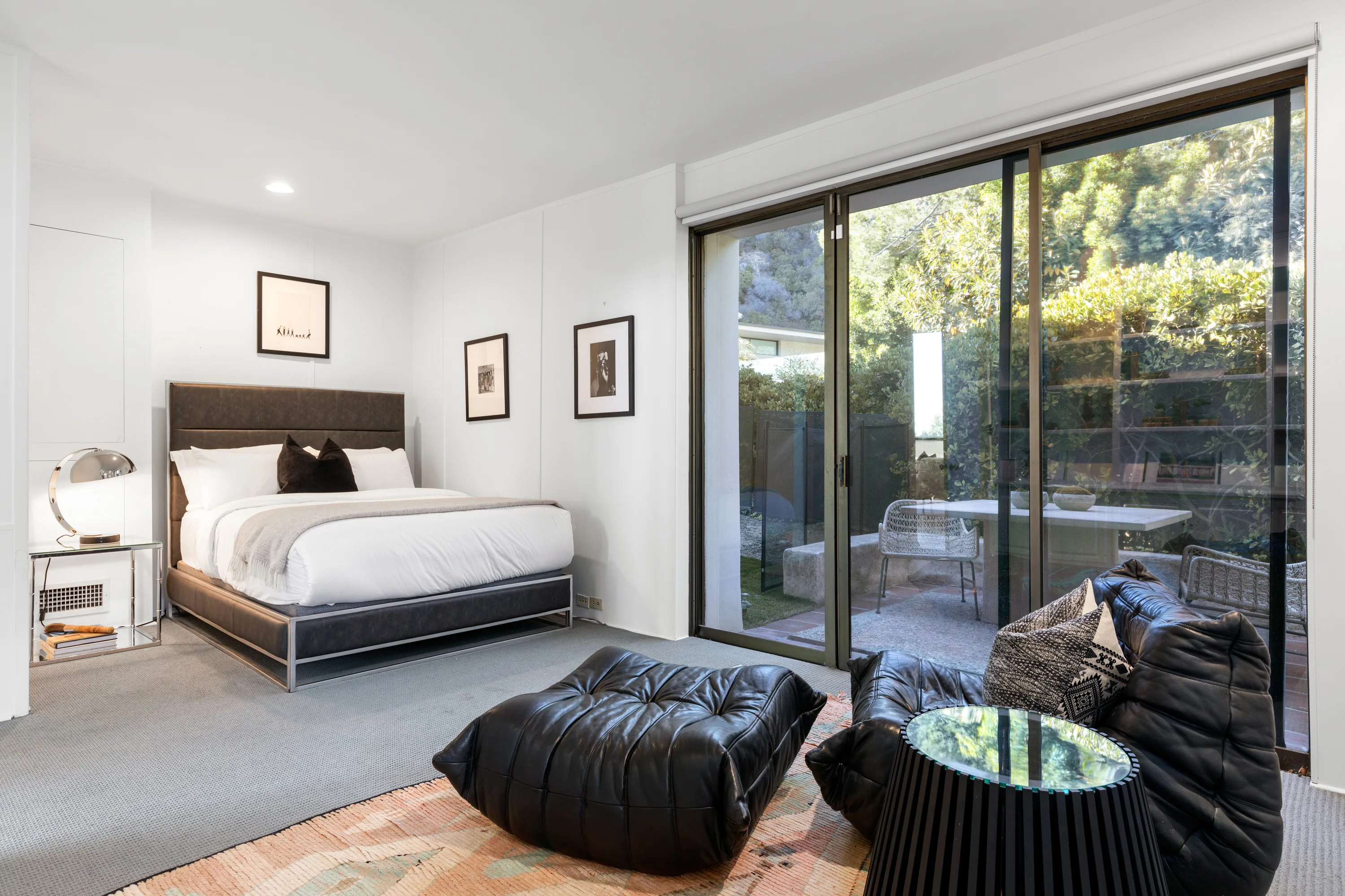 Bedroom suite with leather lounge seating and sliding glass wall onto a hedged patio