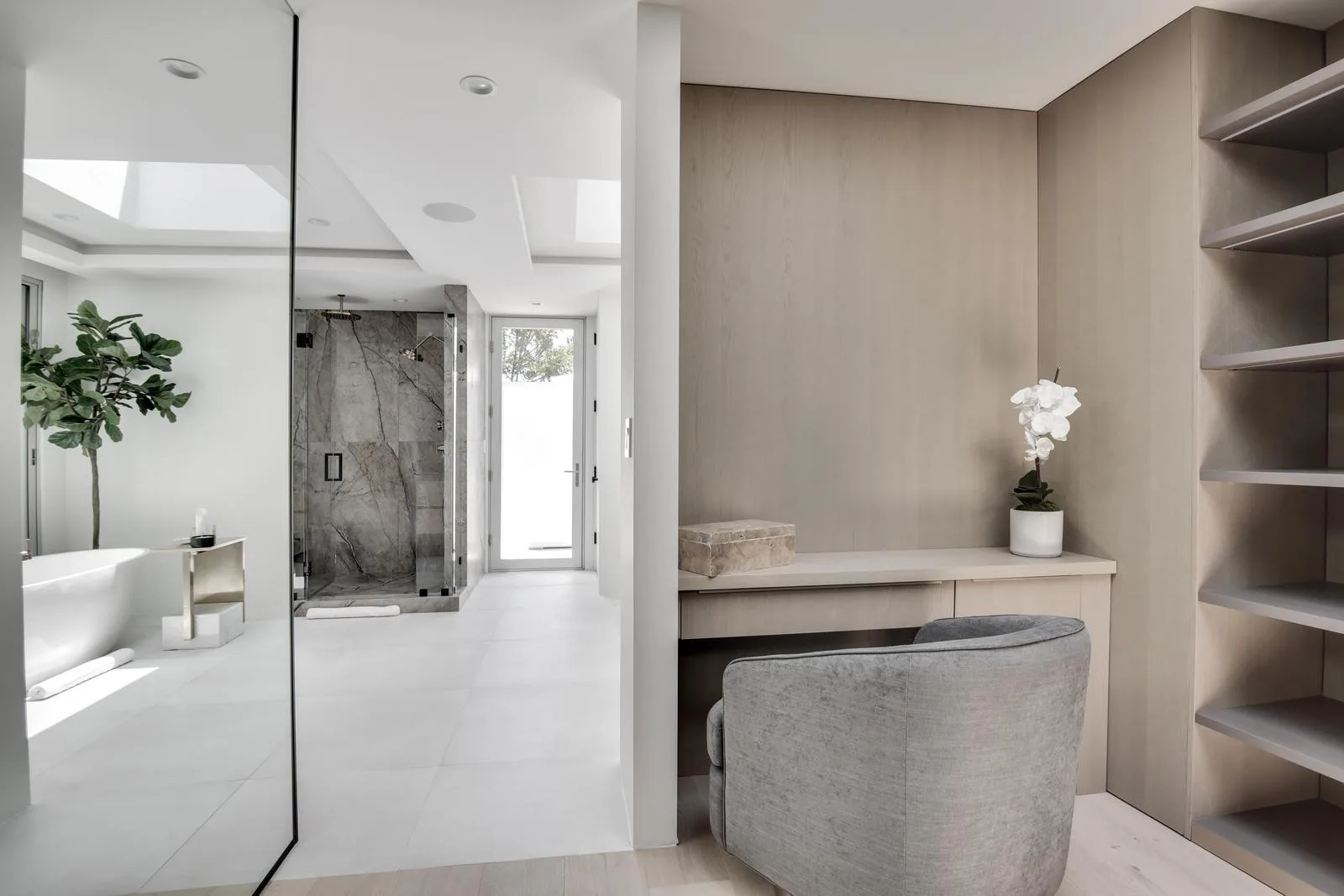 Dressing area with velvet armchair, built-in vanity desk and orchid, opening through to the stone shower