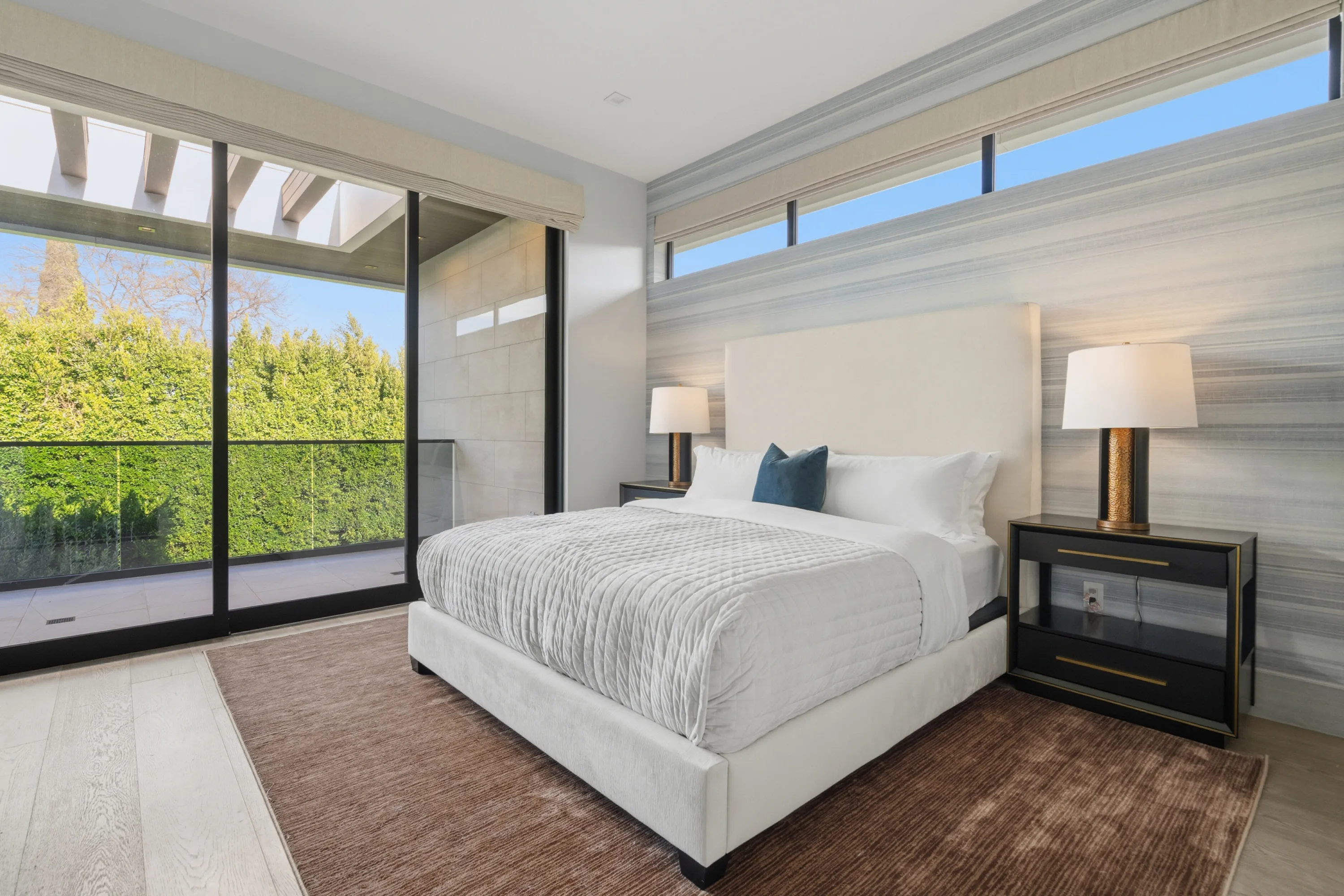 Guest bedroom with upholstered king bed, clerestory windows and sliding glass onto a hedged private deck