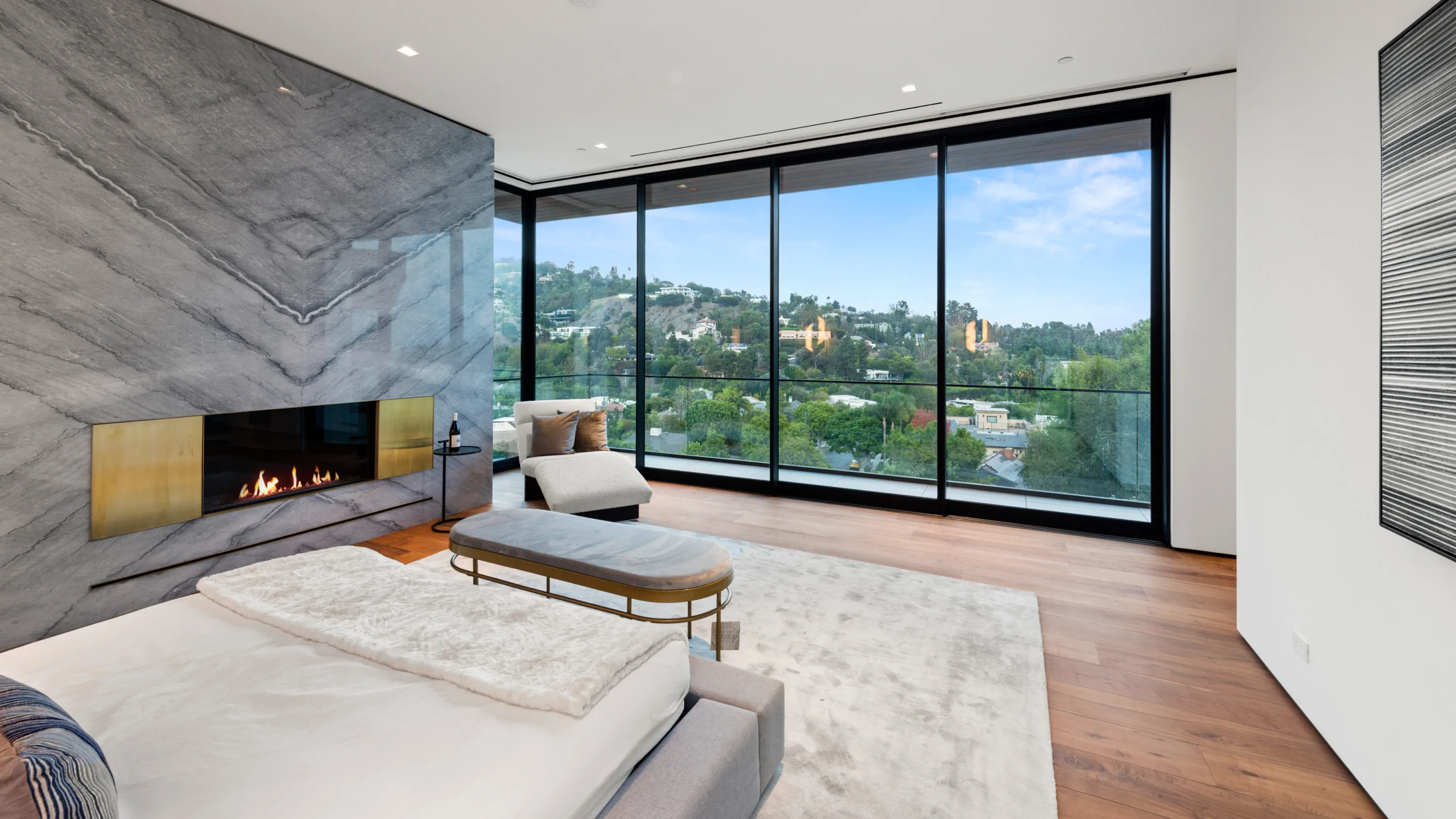 Bedroom fireplace in book-matched grey stone facing floor-to-ceiling glass over the hillside homes