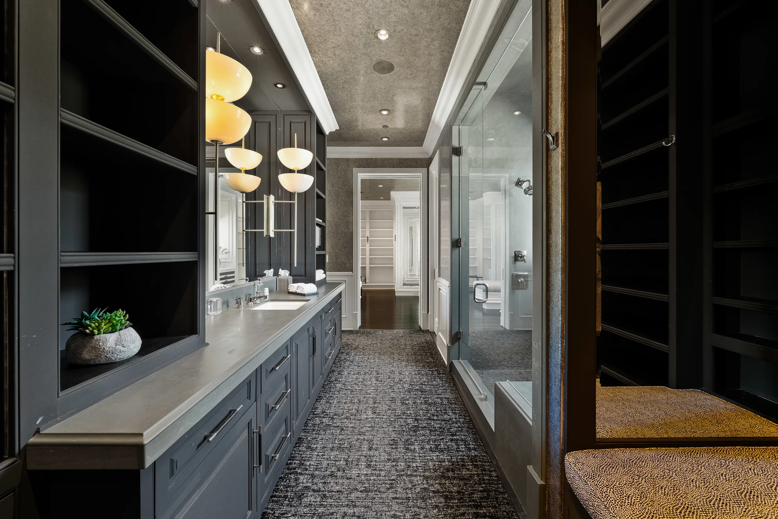 Moody grey vanity run with amber globe sconces, glass shower and open closet shelving beyond
